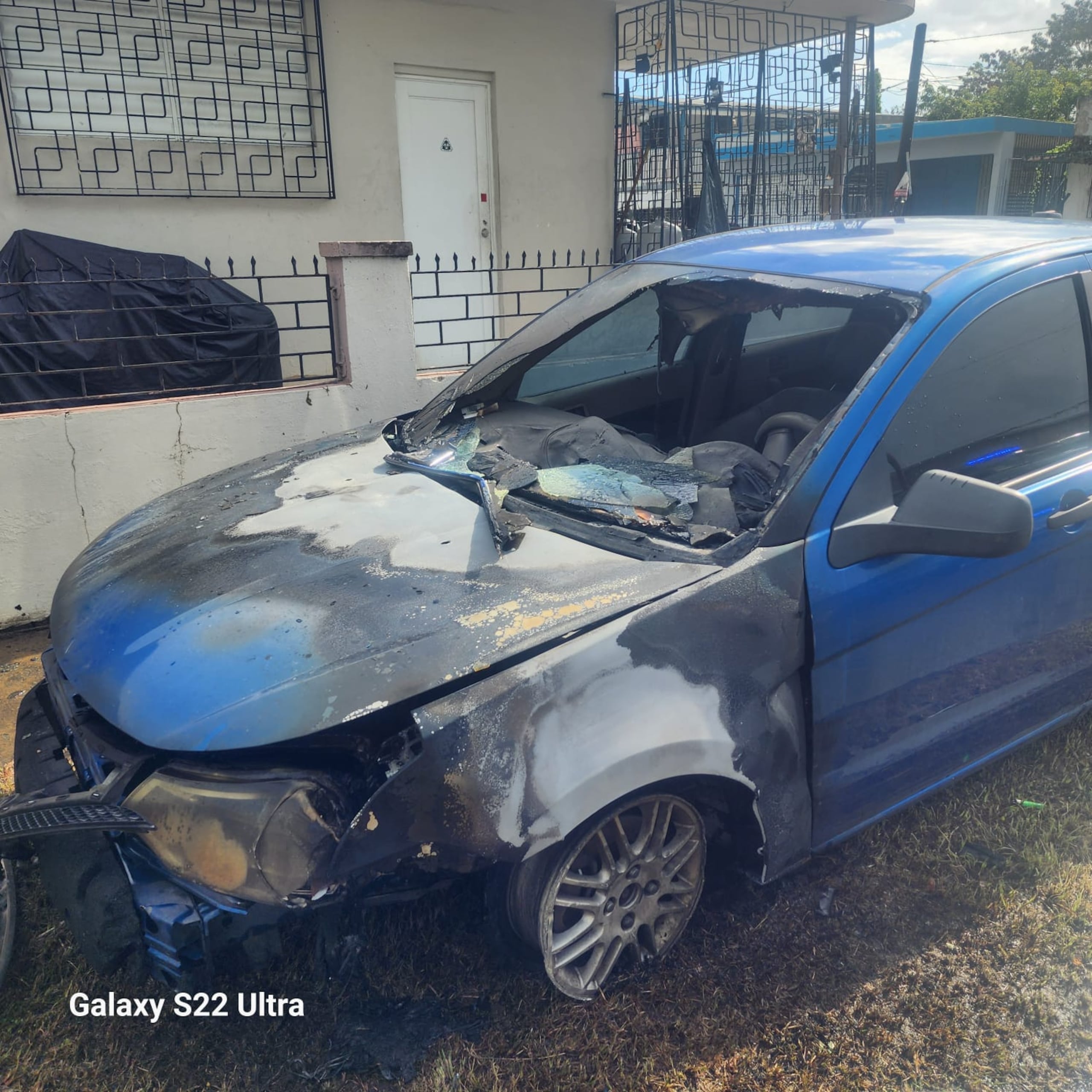 Ford Focus, color azul, del año 2010 y con la tablilla JUE-941, incendiado frente al edificio 18 del residencial Roosevelt, en Mayagüez.