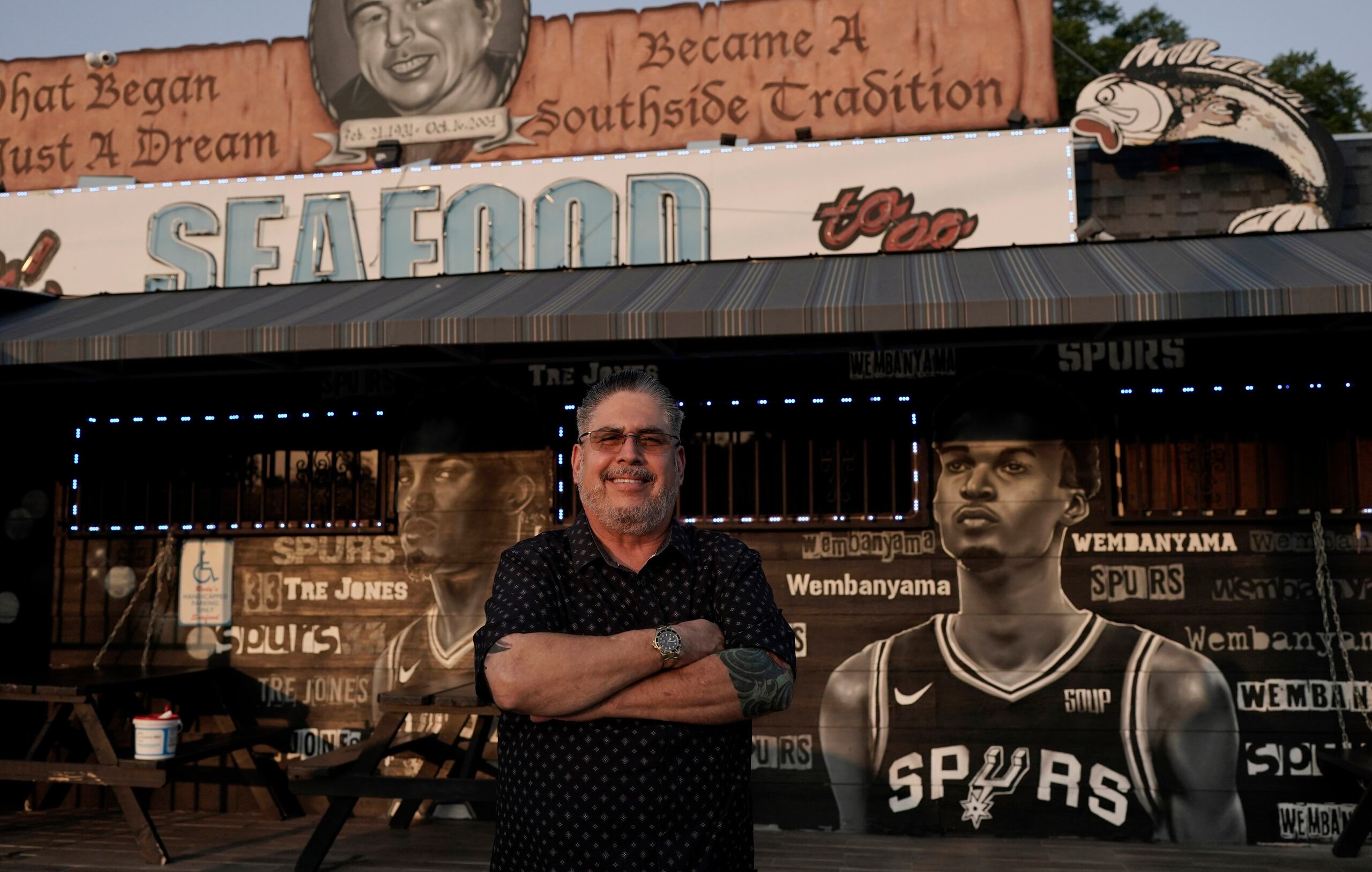 El empresario y seguidor de los Spurs de San Antonio Roland Ramirez posa con el mural del francés Victor Wembanyama que realizó el artista Nik Soupe afuera de su restaurante de mariscos en San Antonio el jueves 15 de junio del 2023. (AP Foto/Eric Gay)