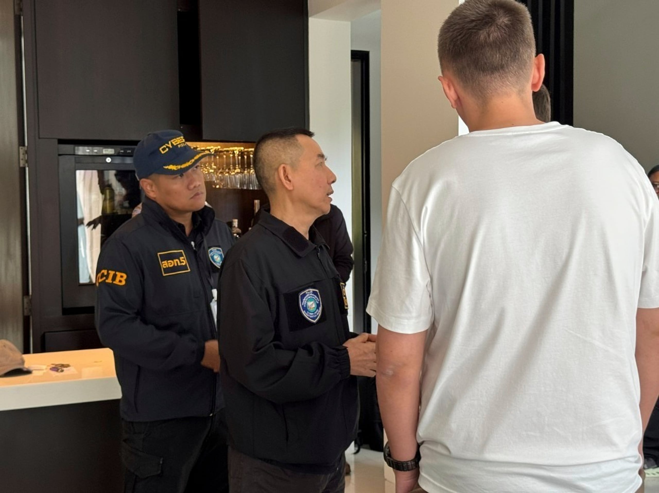 Un presunto hacker ruso de 35 años, identificado por la prensa rusa como Denis Obrezko (derecha, de espaldas), junto a agentes de la policía tailandesa tras haber sido detenido en Phuket, Tailandia, el 6 de noviembre de 2025. (Oficina de Investigación de Ciberdelitos de Tailandia vía AP)