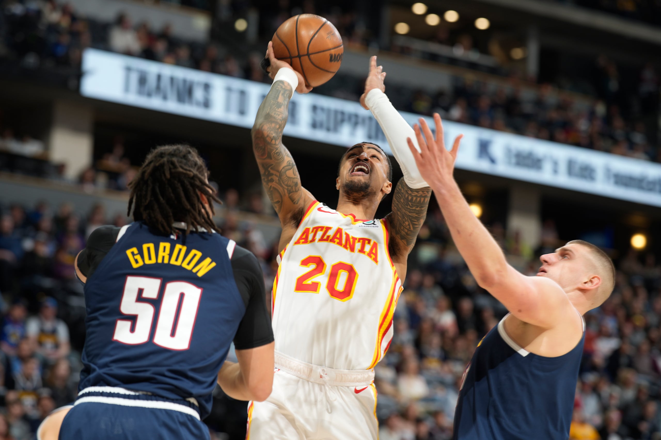 El alero de los Hawks de Atlanta John Collins, al centro, ataca el canasto ante el alero Aaron Gordon y el pívot Nikola Jokic, de los Nuggets de Denver, en la primera mitad del partido del sábado 4 de febrero de 2023, en Denver. (AP Foto/David Zalubowski, Archivo)