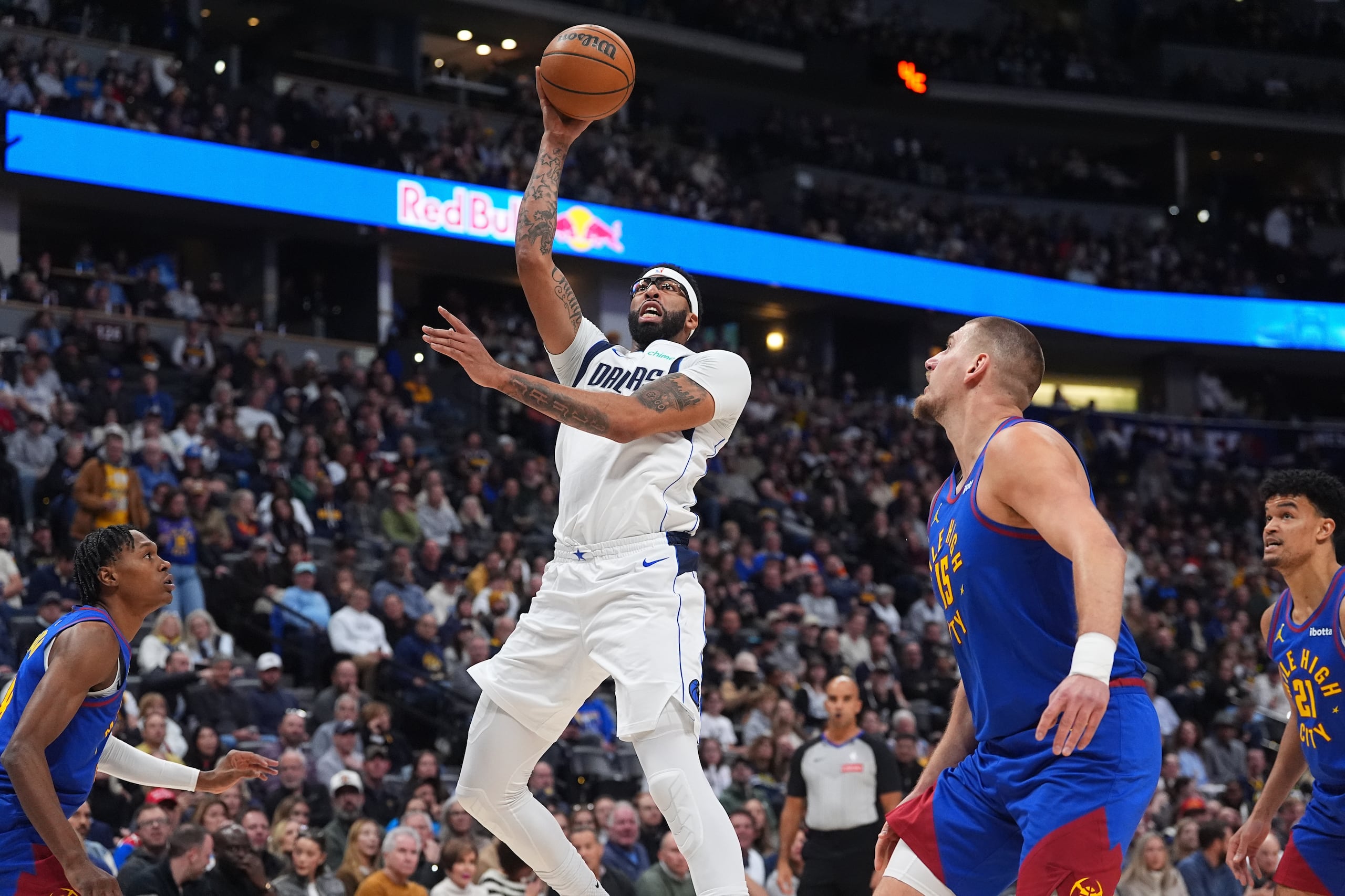 Anthony Davis, pívot de los Mavericks de Dallas, al centro, sube para una canasta mientras Nikola Jokić, pívot de los Nuggets de Denver, al frente a la derecha, defiende en la primera mitad de un juego de baloncesto de la NBA el lunes 1 de diciembre de 2025, en Denver. (AP Photo/David Zalubowski)