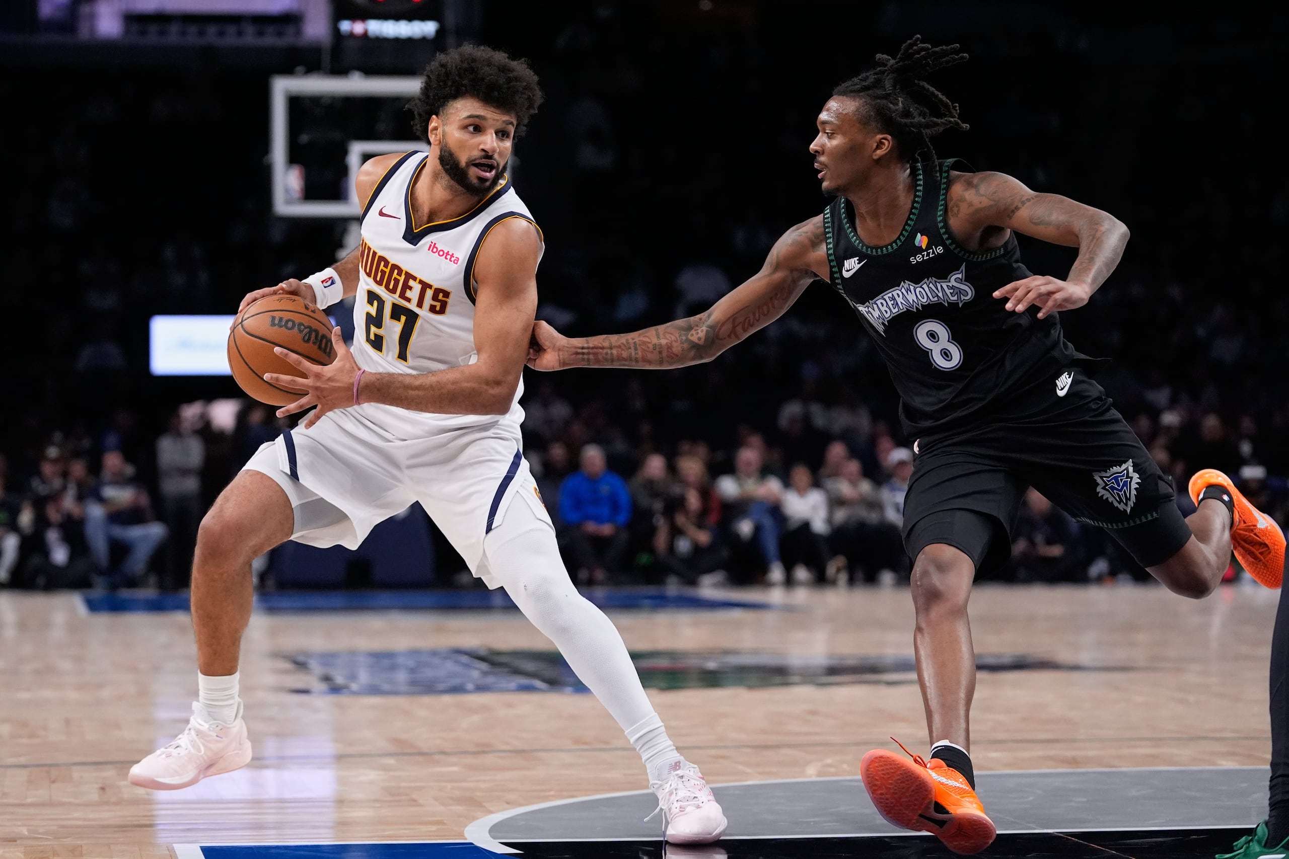 Jamal Murray (27), de los Nuggets de Denver, trabaja para atacar la canasta mientras Bones Hyland (8), de los Timberwolves de Minnesota, defiende durante la segunda mitad del juego de baloncesto de la NBA, el lunes 27 de octubre de 2025, en Minneapolis. (AP Foto/Abbie Parr)