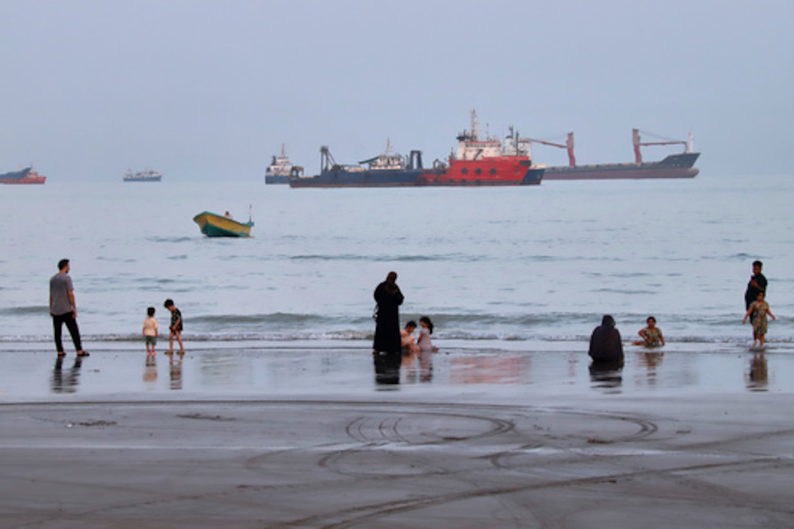 La gente disfruta de la playa mientras varios buques mercantes permanecen fondeados en el estrecho de Ormuz, frente a Bandar Abbas (Irán), el miércoles 5 de agosto de 2026. (Amirhosein Khorgooi/ISNA vía AP)