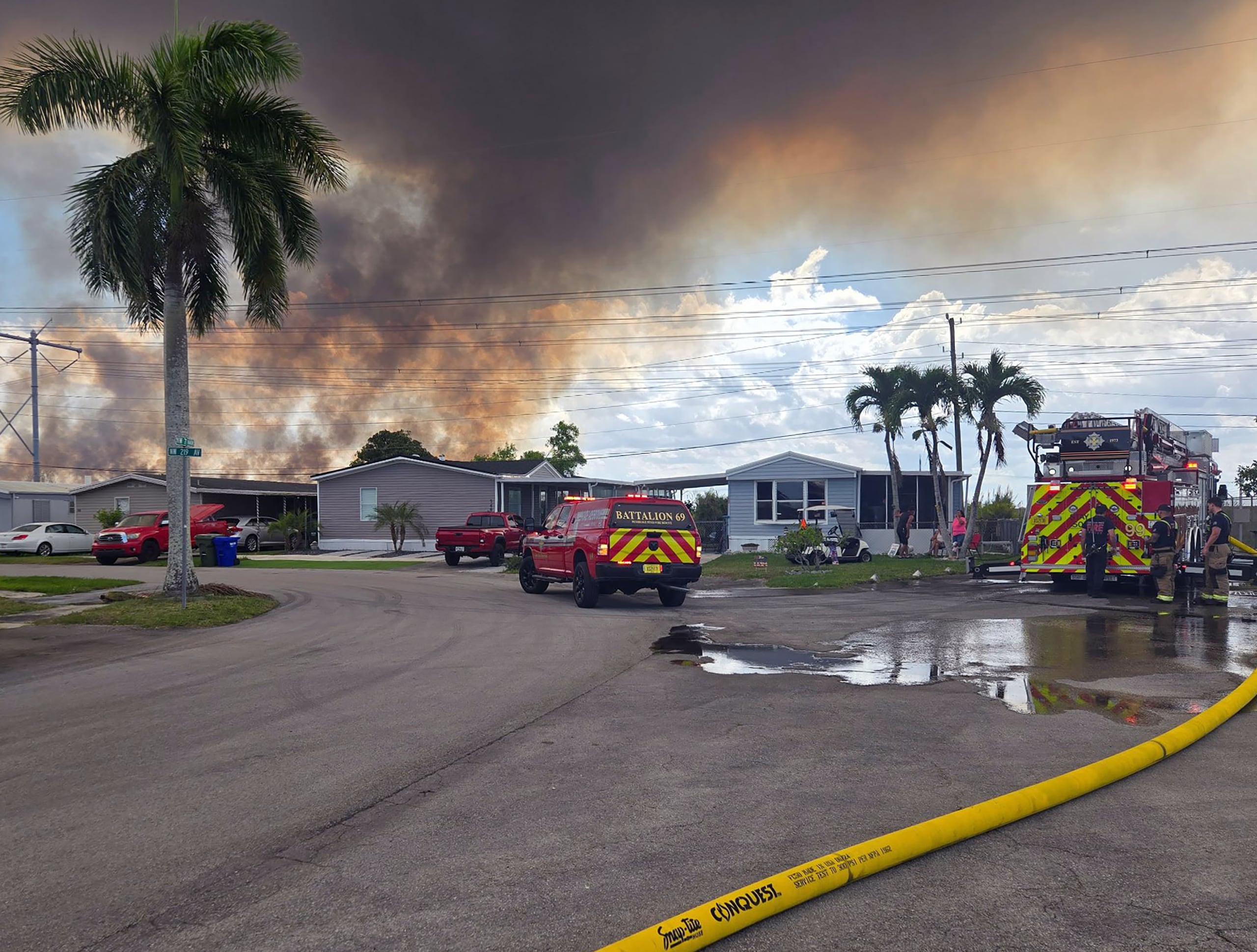 Fotografía divulgada por el Departamento de Policía de Pembroke Pines donde aparecen unos camiones de bomberos abasteciéndose de agua frente a una nube de humo ocasionada por un incendio en los Everglades hacia la zona de Pembroke Pines, Florida.
