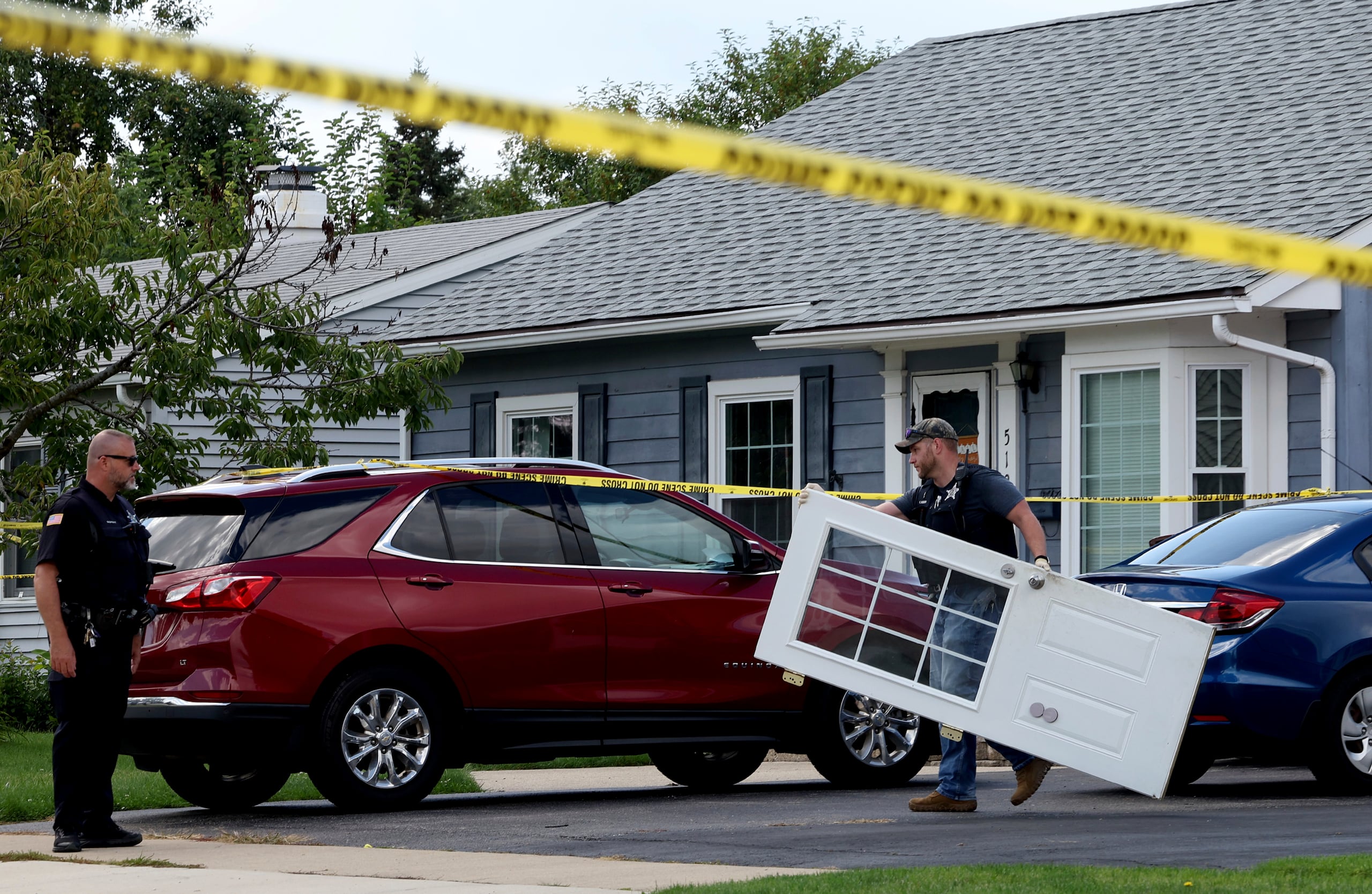 Un oficial de policía de Romeoville carga una puerta de la casa donde la familia fue asesinadas a tiros.
