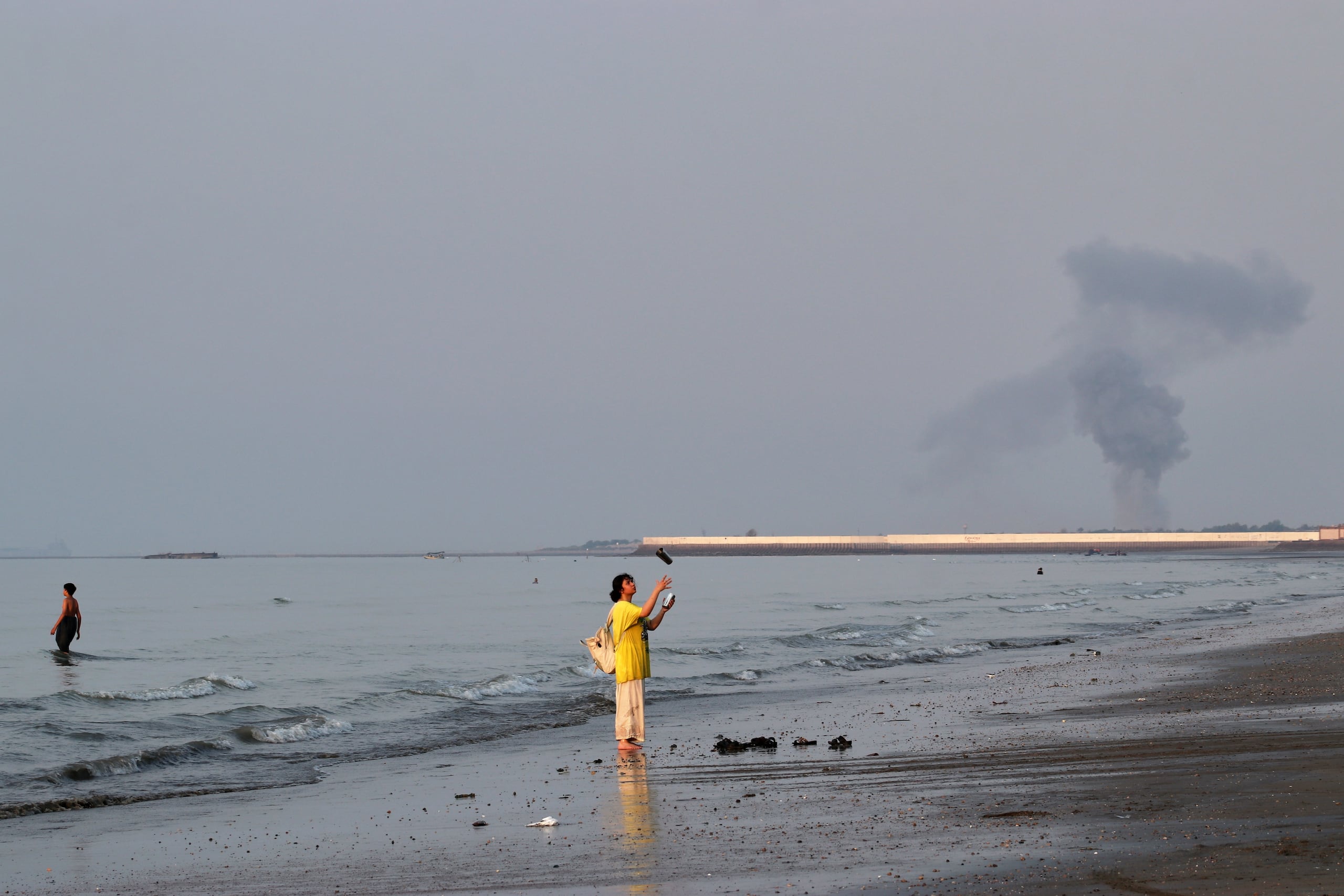 Una mujer cerca de la orilla del mar a lo largo del estrecho de Ormuz, mientras se levanta una columna de humo tras una explosión, frente a Bandar Abbas, Irán, el lunes 13 de julio de 2026. (Razieh Poudat/ISNA vía AP)