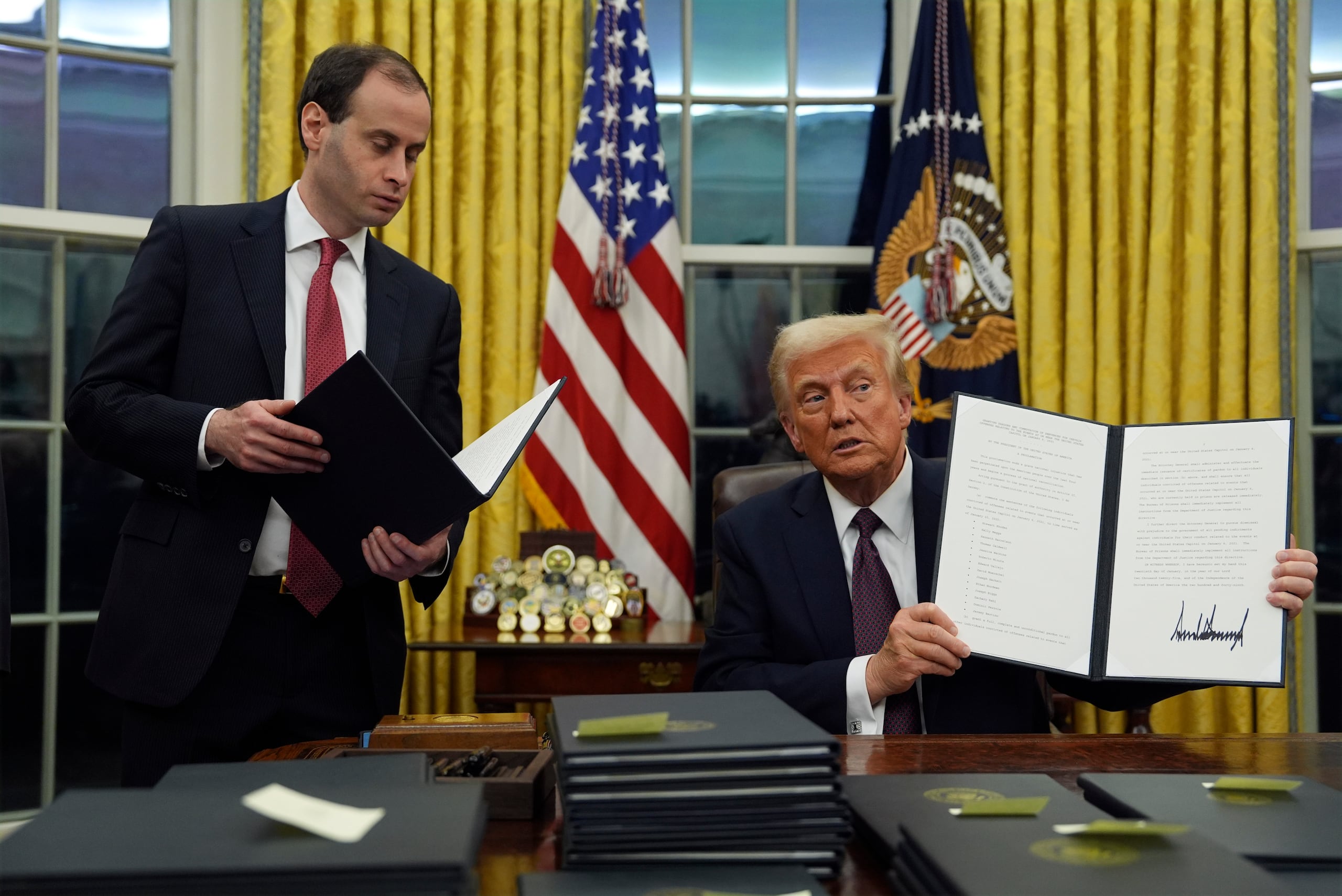 El presidente Donald Trump sostiene una orden ejecutiva que conmuta las sentencias de las personas condenadas por los delitos del 6 de enero en la Oficina Oval de la Casa Blanca, el lunes 20 de enero de 2025, en Washington. (Foto AP/Evan Vucci)