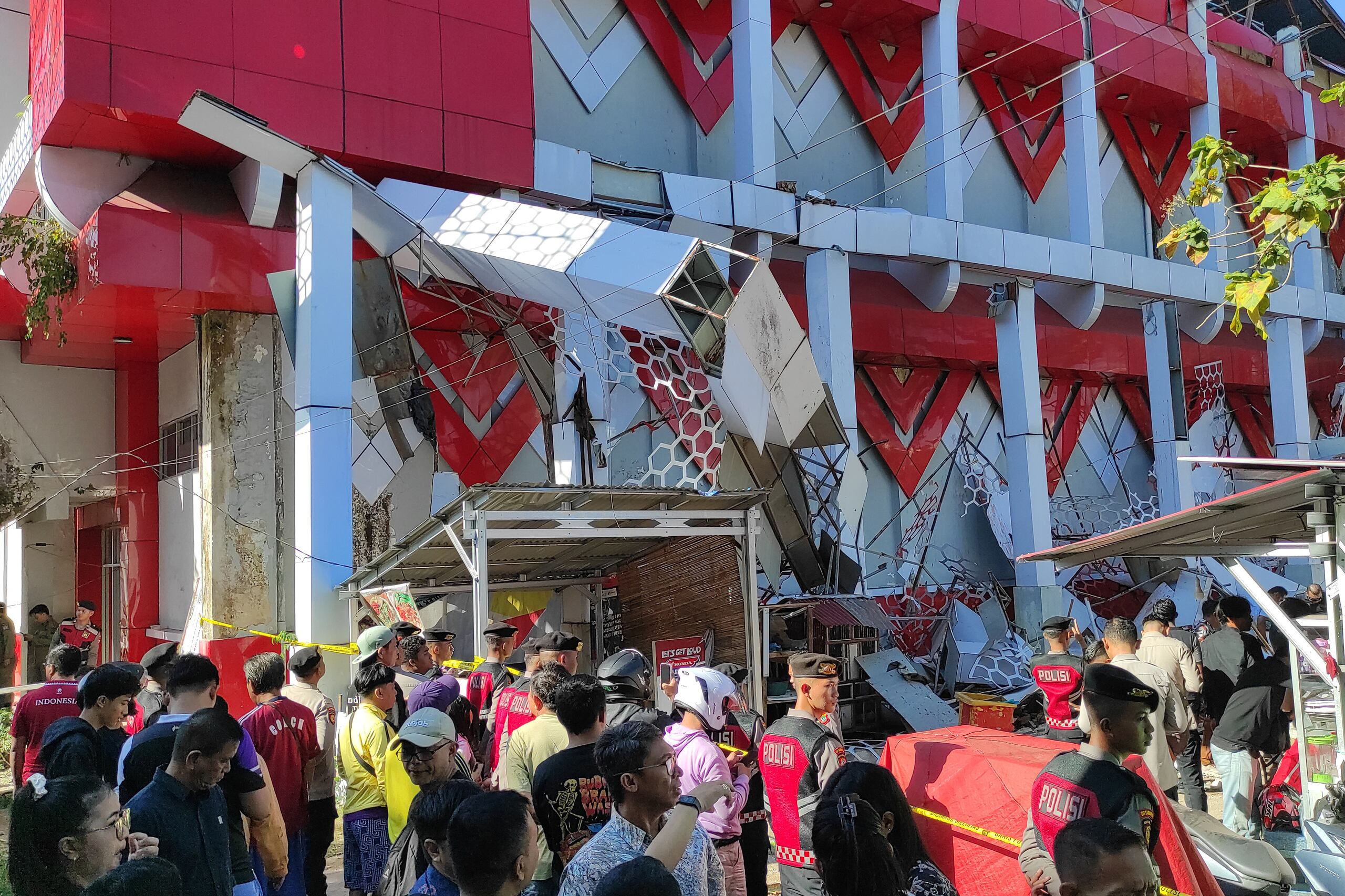 Personas observan mientras policías revisan un edificio dañado por un sismo, el jueves 2 de abril de 2026, en Manado, Célebes Septentrional, Indonesia. (AP Foto/Tonny Rarung)