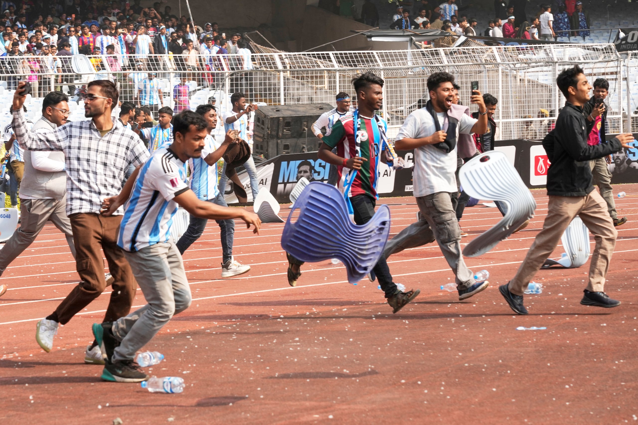Aficionados indios arrancan las sillas en su carrera hacia el césped tras no haber podido ver al astro argentino Lionel Messi en el estadio Salt Lake, en Calcuta, India, el 13 de diciembre de 2025. (AP Foto/Bikas Das)
