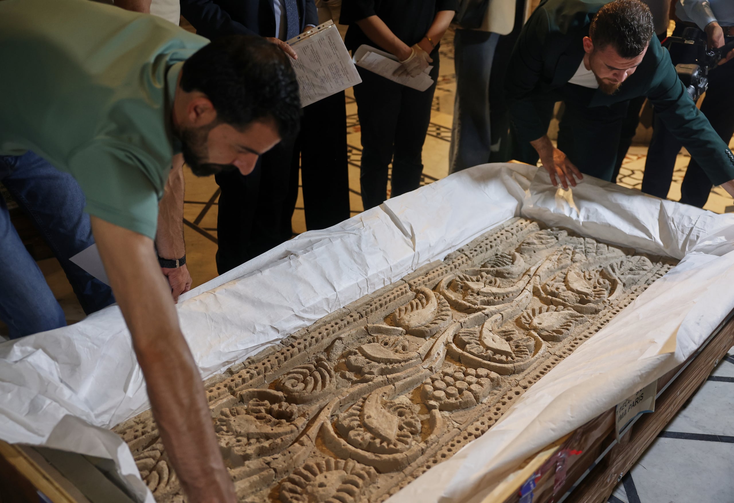 Varios empleados desempacan un panel de piedra labrada después de que autoridades sirias revelaran las antigüedades devueltas por Francia, en el Museo Nacional en Damasco, Siria, el miércoles 8 de julio de 2026. (AP Foto/Ghaith Alsayed)