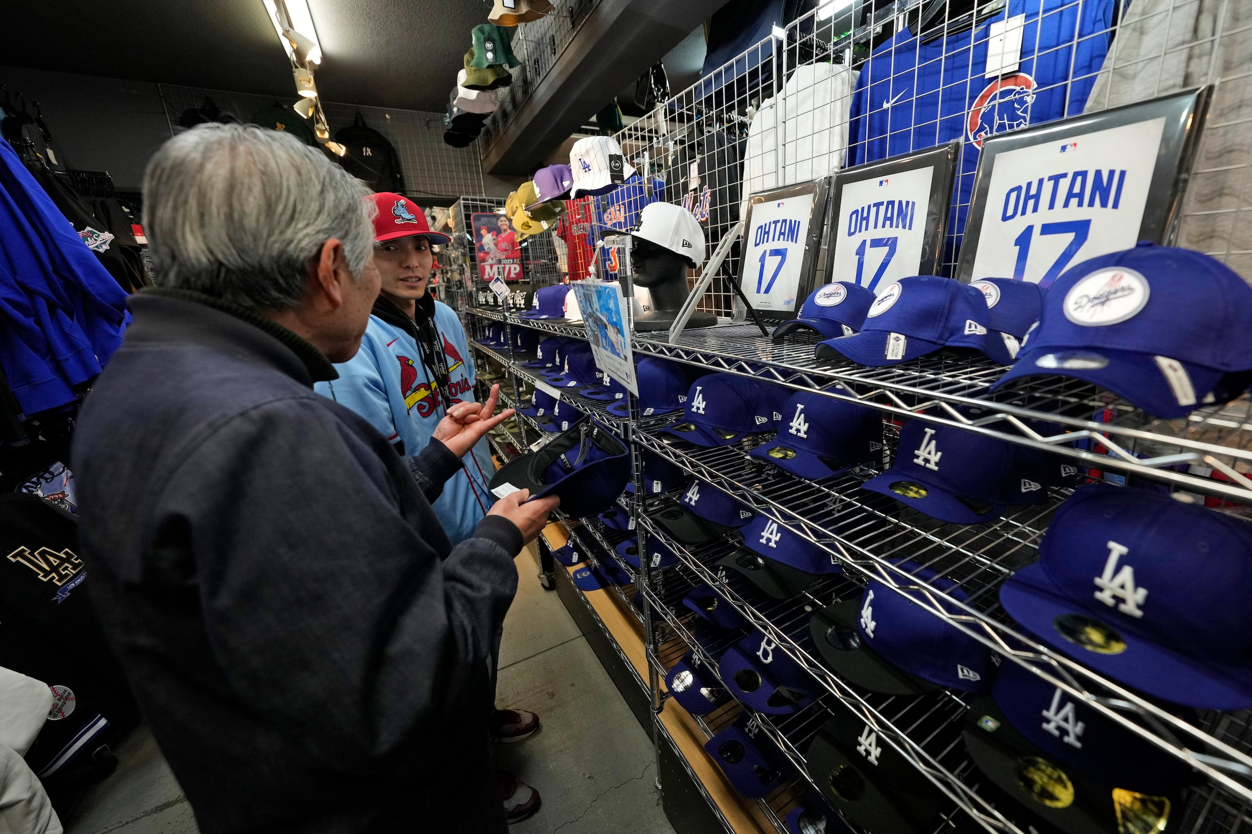 Un trabajador de la tienda le ayuda a un comprador a elegir gorras de béisbol con diferentes diseños con el nombre de Shohei Ohtani en una tienda en Tokio, Japón el 29 de febrero del 2024.