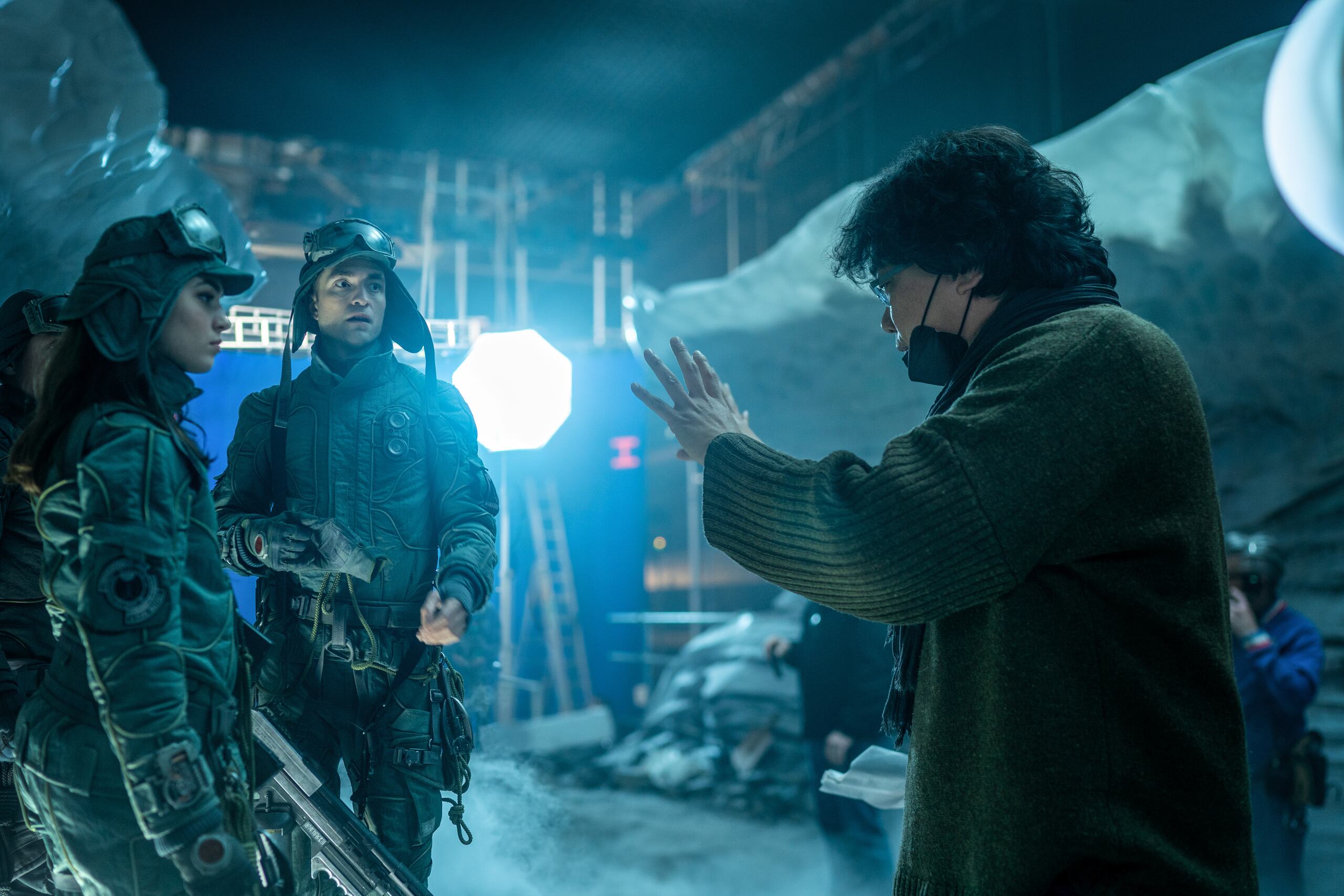 El director de cine surcoreano Bong Joon-ho (d) conversa con los actores Robert Pattison y Anamaria Vartolomei durante el rodaje de 'Mickey 17'.