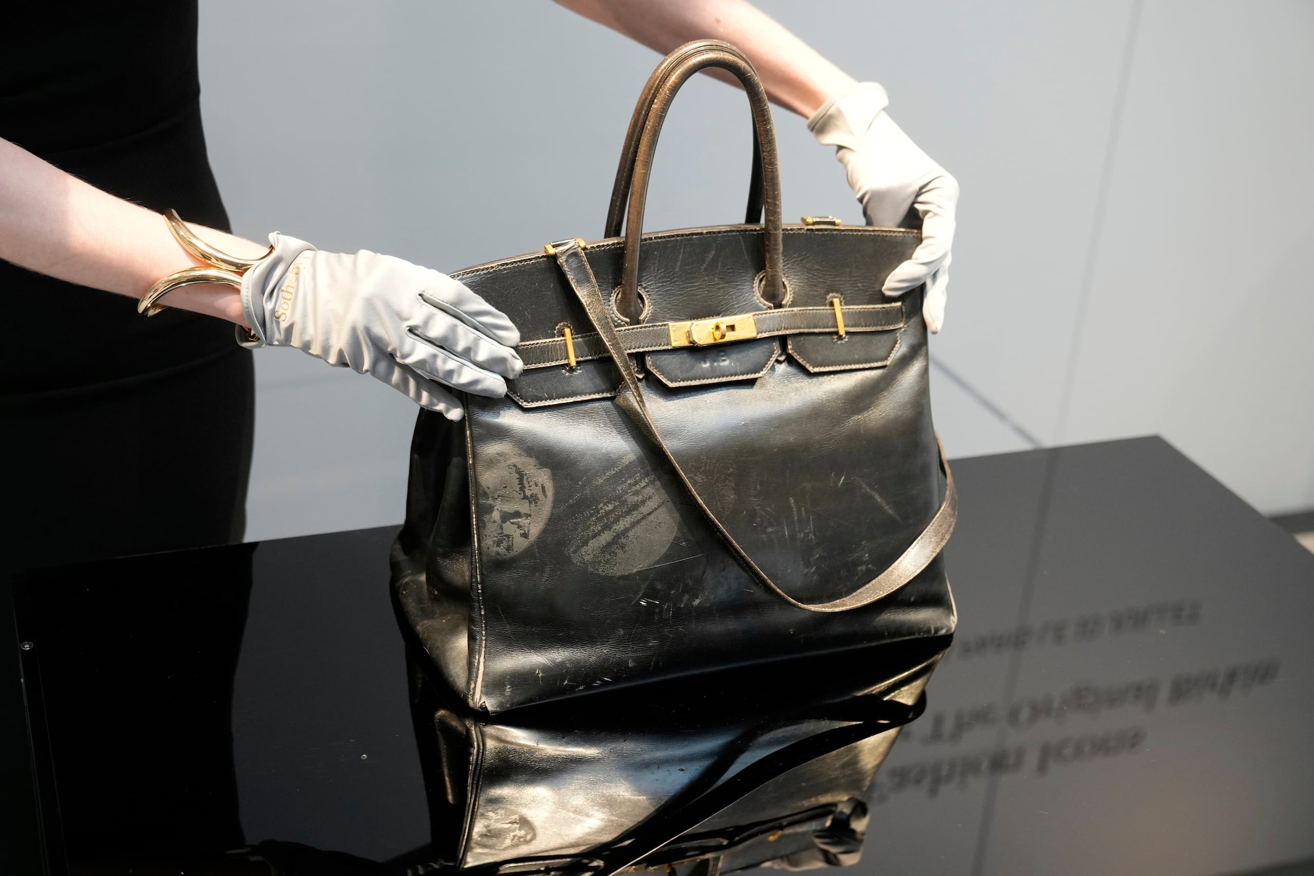 Un oficial de subasta muestra el bolso Birkin original creado por Hermès para Jane Birkin en 1984, antes de su subasta el jueves 10 de julio de 2025 en París. (AP Photo/Michel Euler)