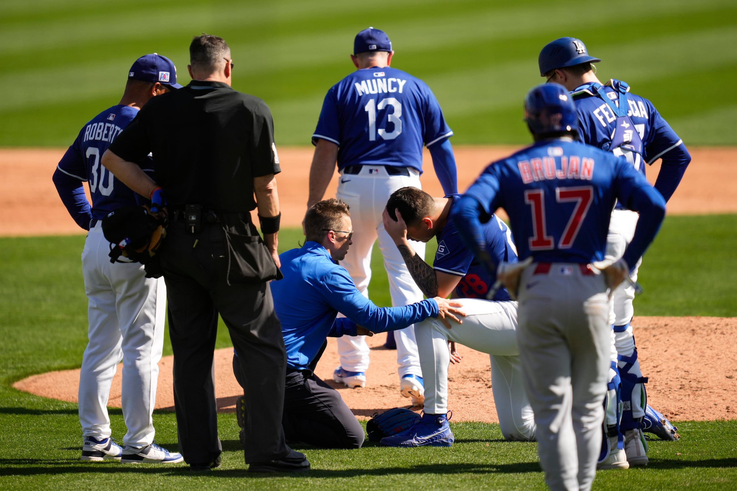 Bobby Miller, de rodillas, lanzador de los Dodgers de Los Ángeles, reacciona después de recibir un batazo en la cabeza con una línea de Michael Busch, de los Cubs de Chicago, durante la tercera entrada de un juego de entrenamiento de primavera, el jueves 20 de febrero de 2025, en Phoenix.