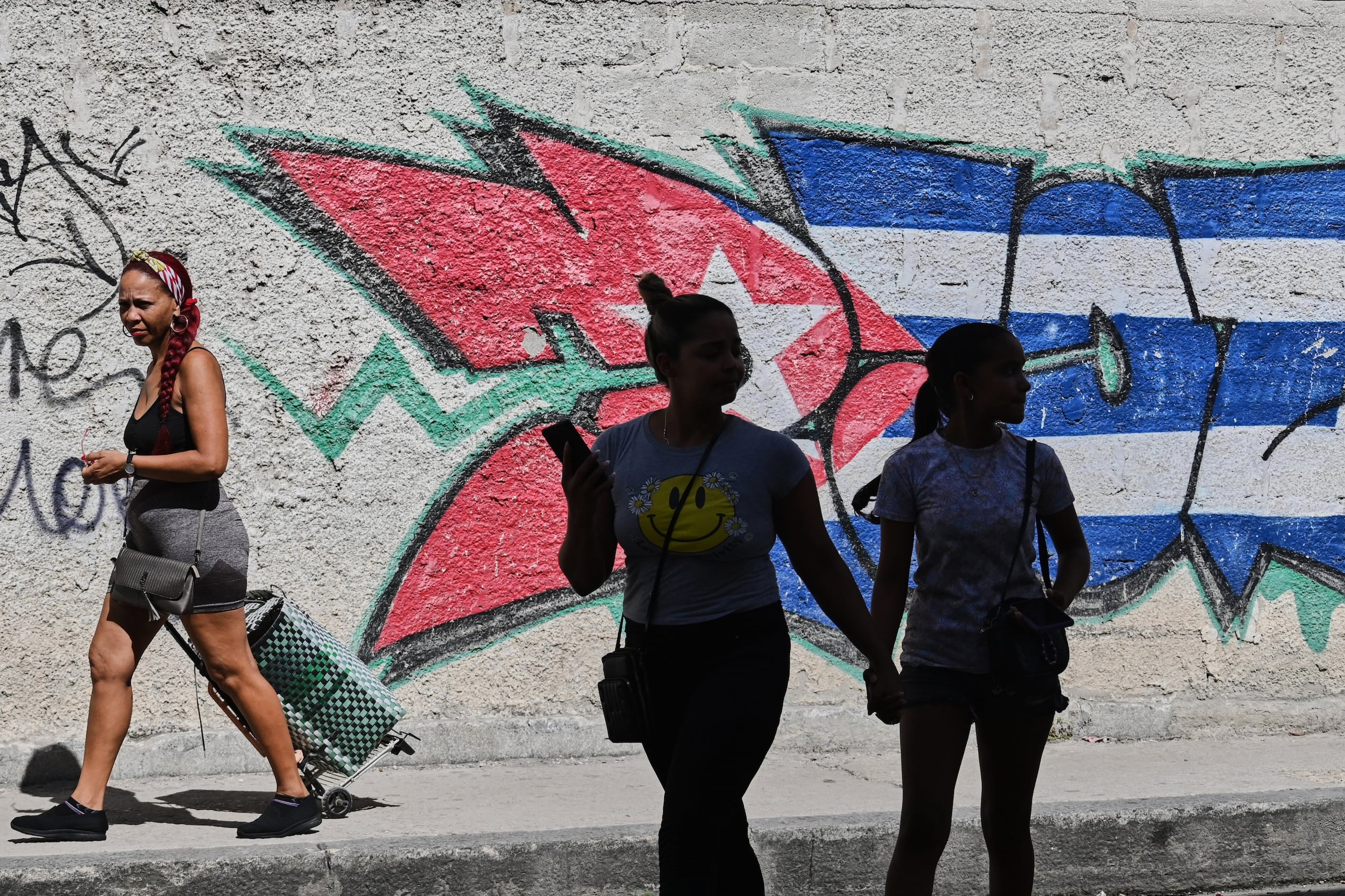 Varias personas pasan junto a grafitis con los colores de la bandera cubana en La Habana, Cuba, el miércoles 17 de junio de 2026. (Foto AP/Jorge Luis Banos)