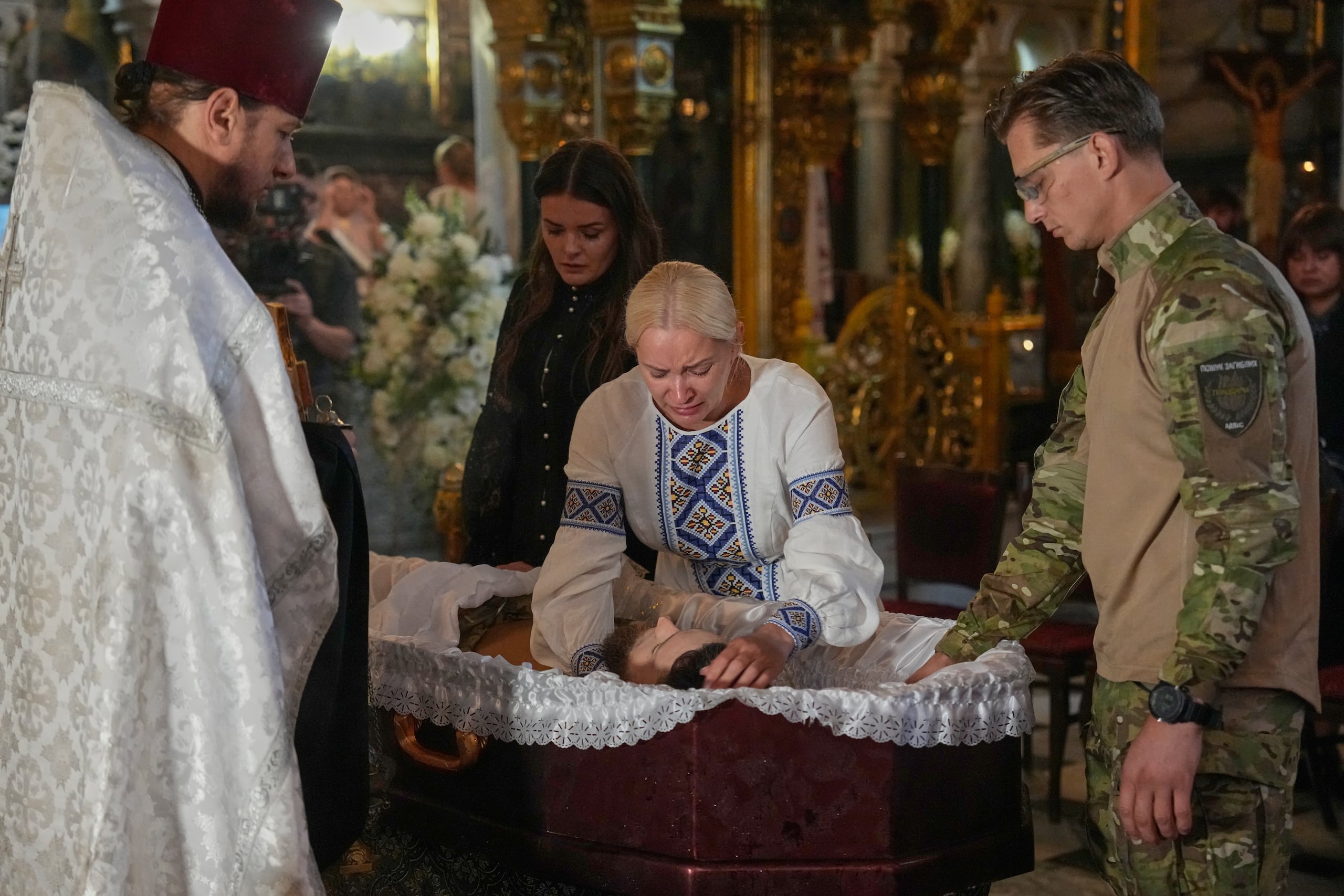 Familiares lloran junto al ataúd de Oleksiy Yukov, quien resultó herido de muerte mientras exhumaba los cuerpos de soldados caídos en el frente en la región de Donetsk, durante el funeral celebrado en la catedral de San Volodymyr en Kiev, Ucrania, el sábado, 8 de agosto. (Foto AP/Efrem Lukatsky)