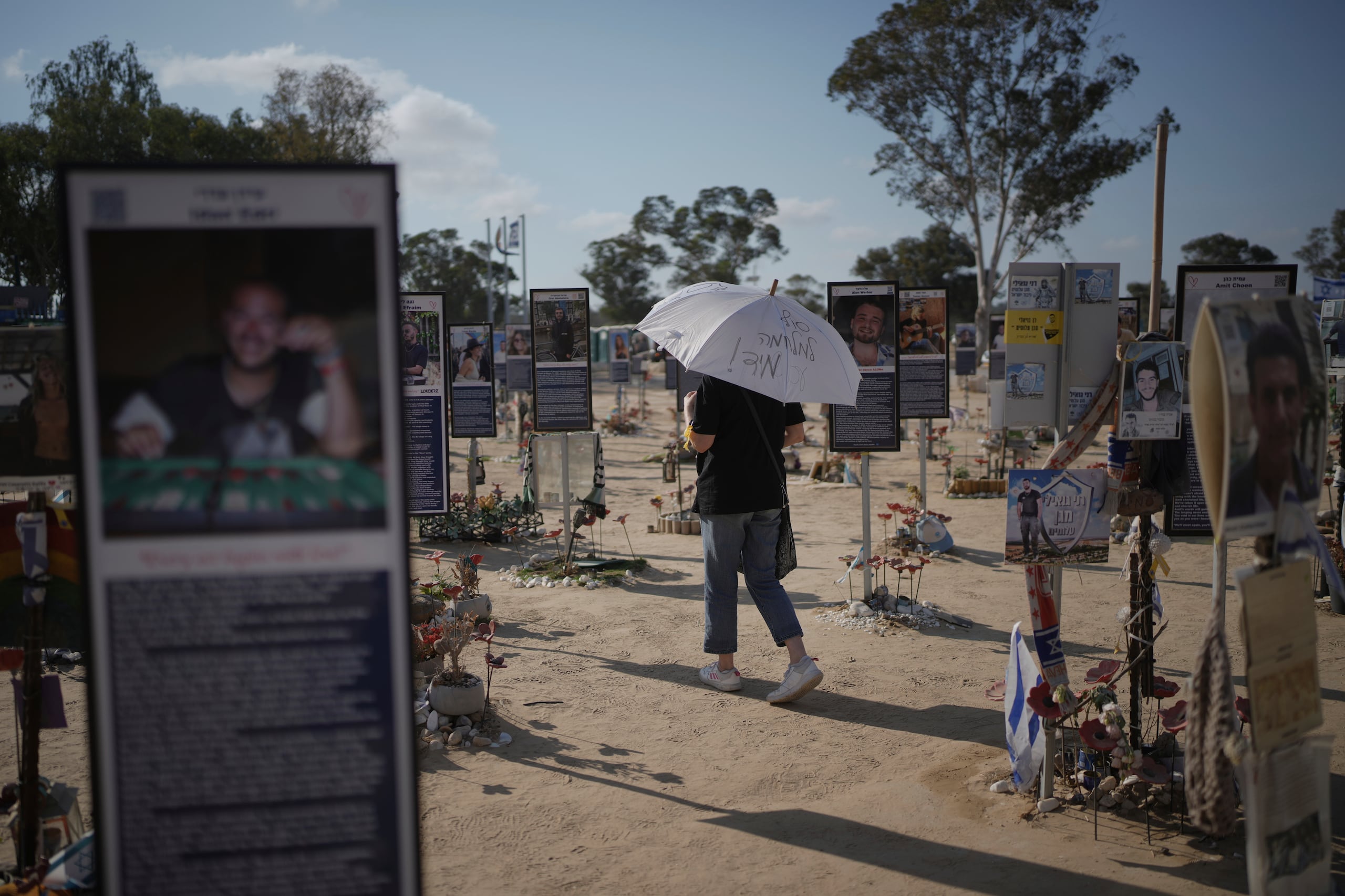 Una mujer camina con un paraguas y lee "Fin a la guerra de inmediato" durante una protesta para exigir la liberación inmediata de los rehenes retenidos por Hamás en la Franja de Gaza, en el lugar del ataque de Hamás del 7 de octubre de 2023 contra el festival de música Nova, cerca del kibutz Reim, en el sur de Israel, el miércoles 2 de julio de 2025. (Foto AP/Ohad Zwigenberg)