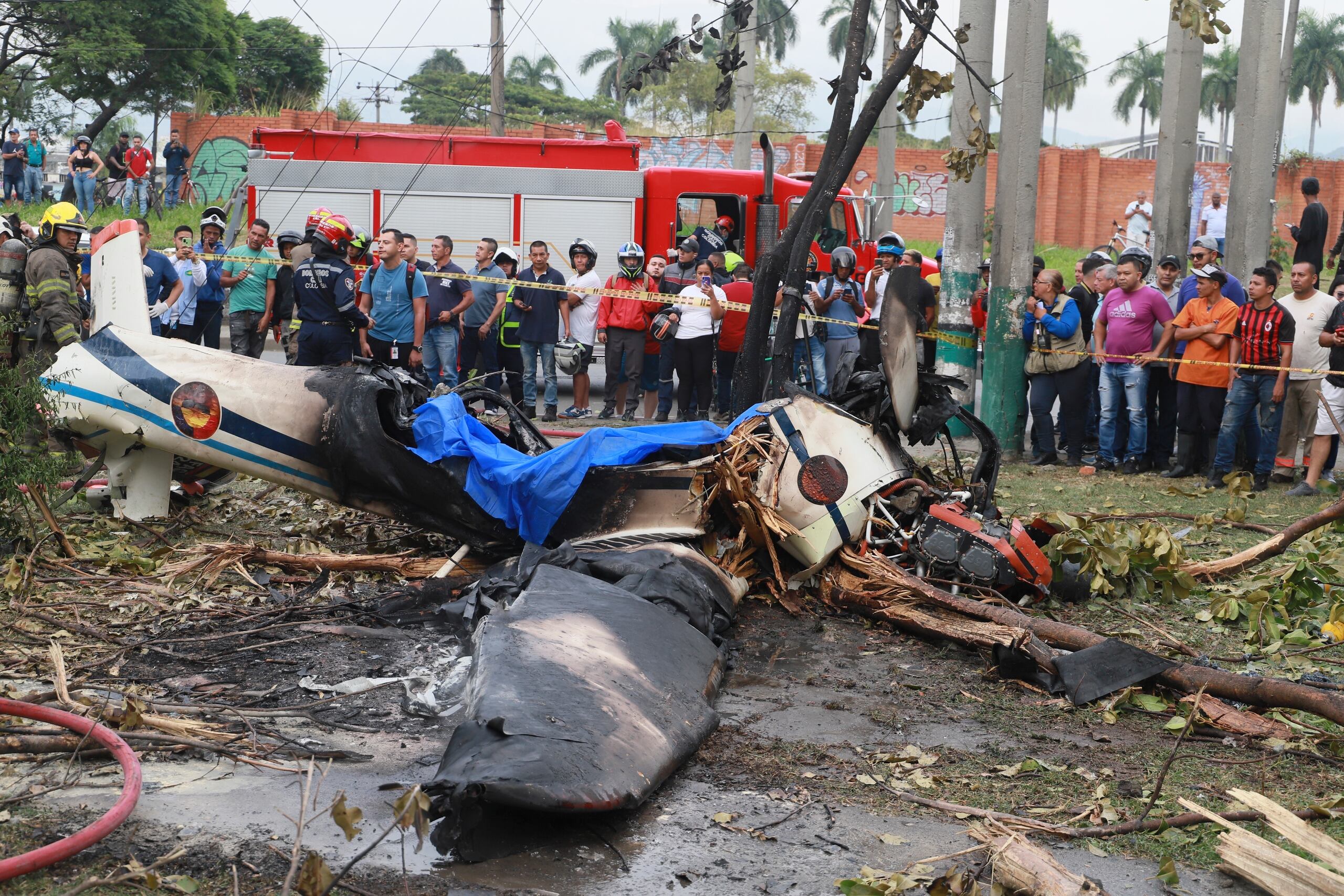 Residentes observan los restos de un avión de una escuela de la Fuerza Aeroespacial Colombiana que se estrelló en un área urbana de Cali, Colombia, el martes 3 de octubre de 2023. Según las autoridades, una persona a bordo murió y otra resultó herida. (AP Foto/Juan B. Díaz)