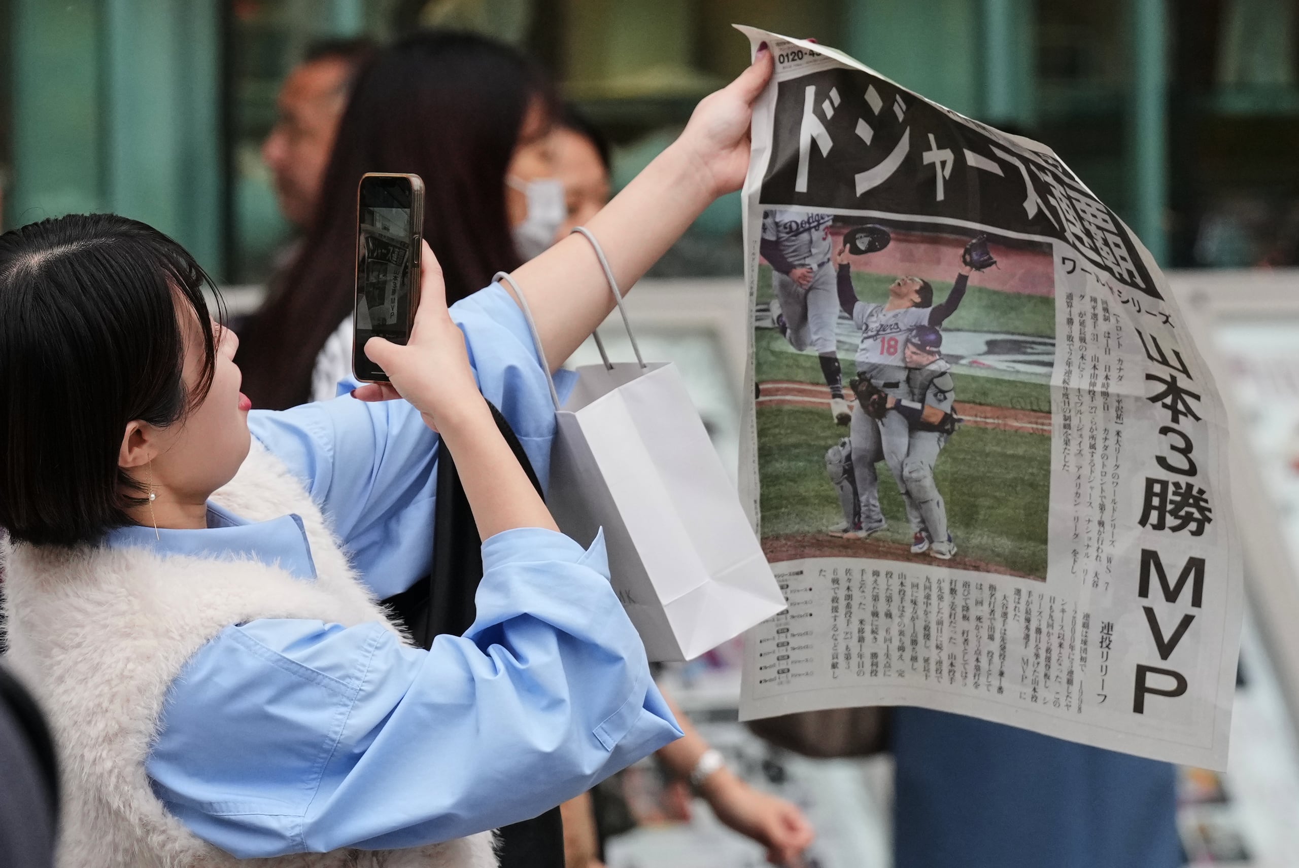 Una mujer en Tokio toma una foto de la edición extra del periódico con la victoria de los Dodgers de Los Ángeles.