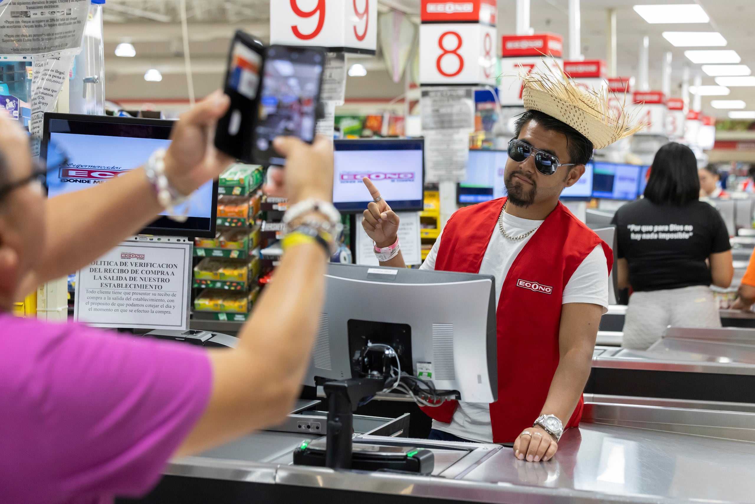Un participante en una visita guiada posa en la caja número 10 del supermercado en el que Bad Bunny solía trabajar en Vega Baja, Puerto Rico, el 12 de agosto de 2025. (AP Foto/Alejandro Granadillo)