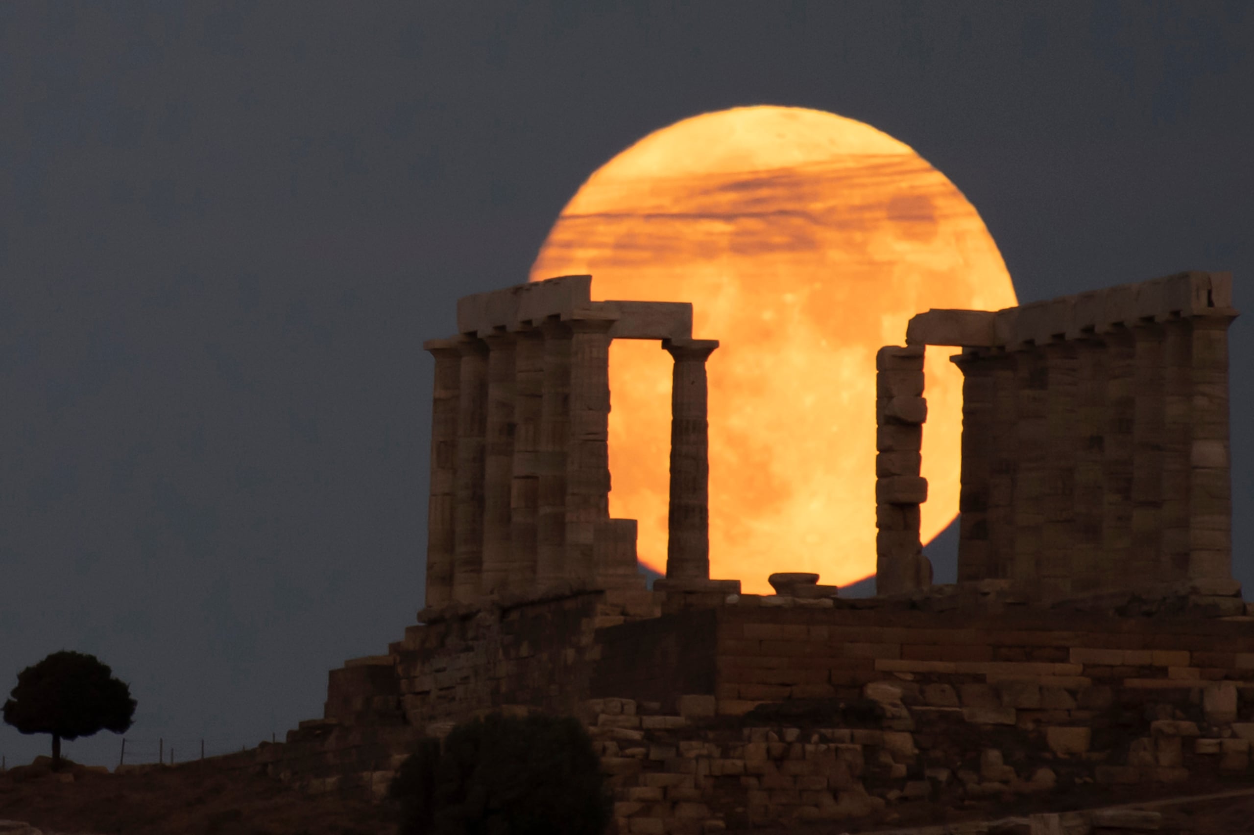 The sturgeon full moon rises behind the ancient Greek marble temple of Poseidon at Cape Sounion, about 70 Km (45 miles) south of Athens, Saturday, Aug. 21, 2021. On Sunday, more than a hundred archeological sites and museums across the country will welcome the public to admire the full moon. (AP Photo/Michael Varaklas)