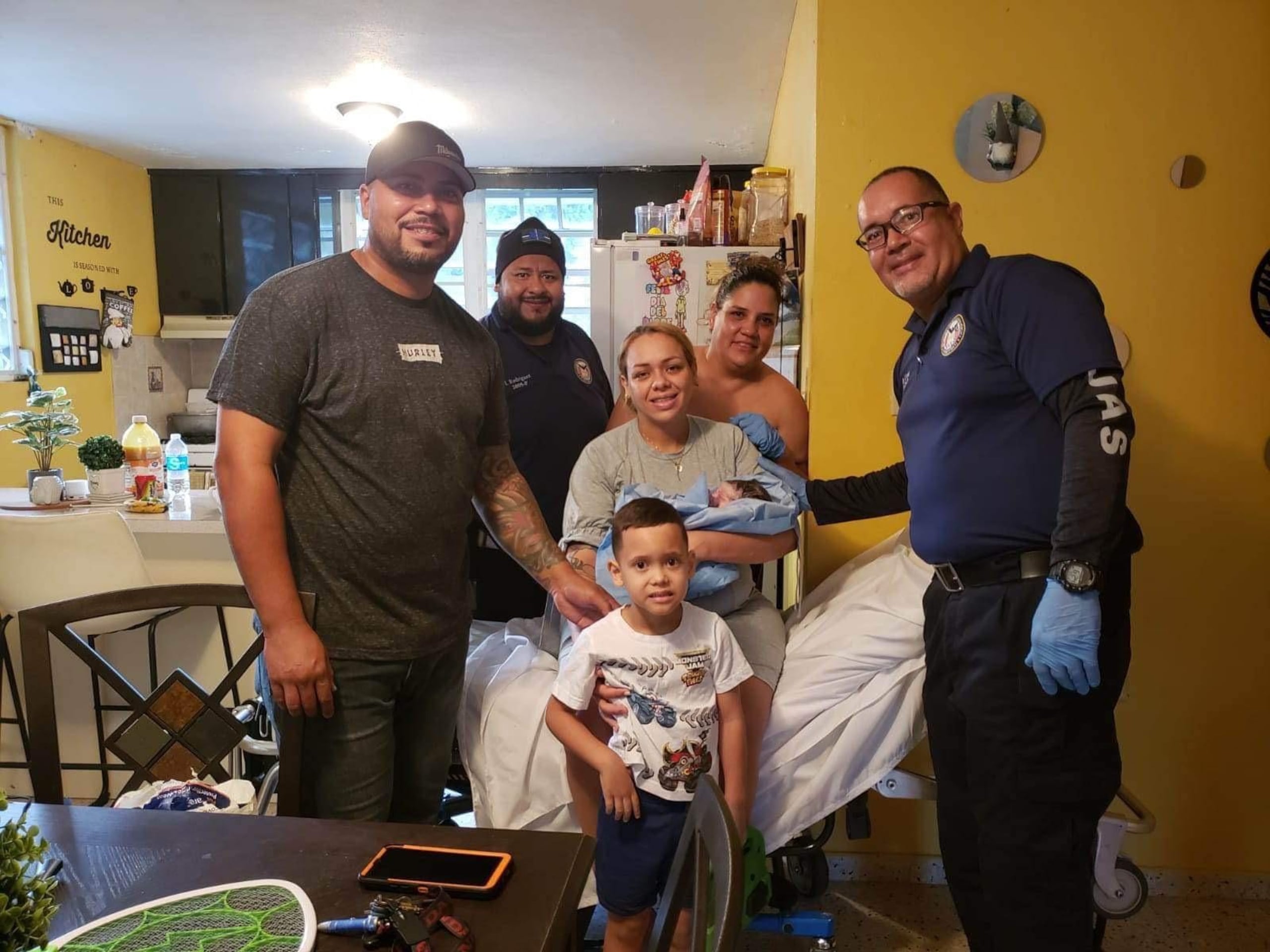 Iván Rodríguez (al fondo) y David Cruz (a la derecha), del Negociado del Cuerpo de Emergencias Médicas, posan con la familia Ortiz Ramírez en su residencia en Lajas.
