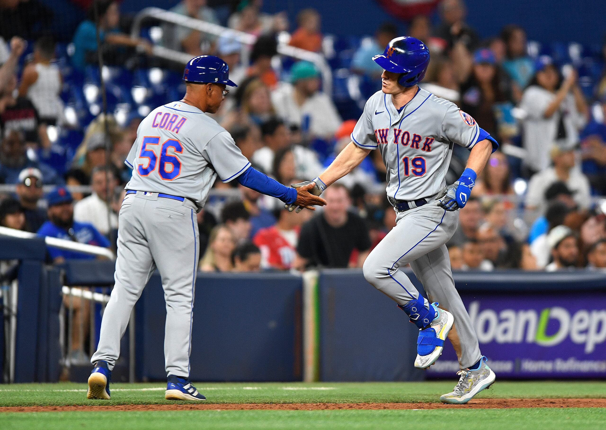 Mark Canha (19), de los Mets, choca manos con el coach de tercera base de la novena, el boricua Joey Cora, luego de sacudir un cuadrangular ante los Marlins de Miami.