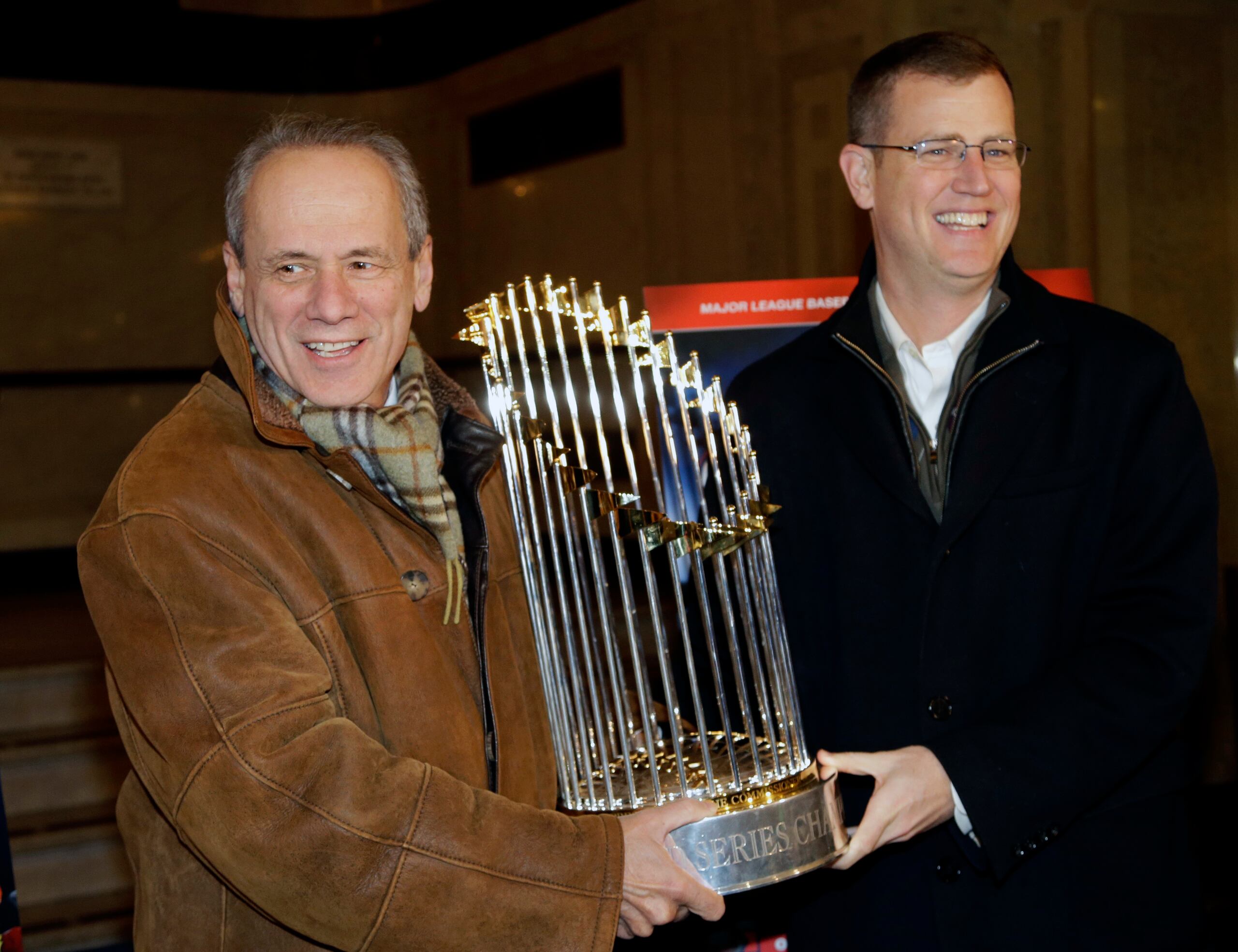 Larry Lucchino, a la izquierda, sostiene junto al Principal Oficial de Operaciones, Sam Kennedy, el trofeo de la Serie Mundial del 2013, uno de los que será subastado. Lucchino murió en abril pasado.
