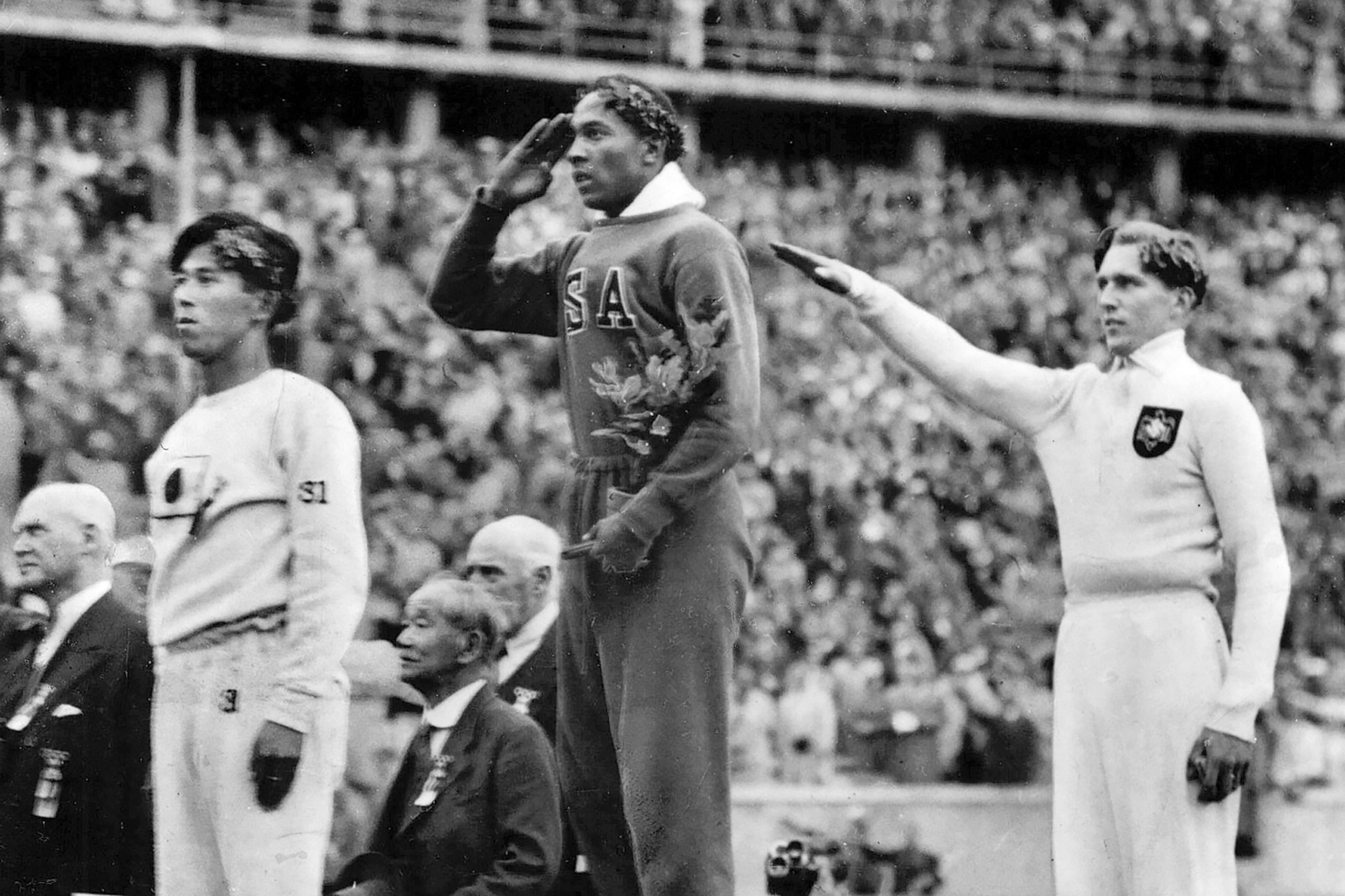 ARCHIVO - Foto del 11 de agosto de 1936, el estadounidense Jesse Owens saluda durante la presentación por la medalla de oro en salto de longitud en los Juegos Olímpicos al lado del medallista de plata, el alemán Luz Long y el medallista de bronce Noato Tajima de Japón. (AP Foto/Archivo)