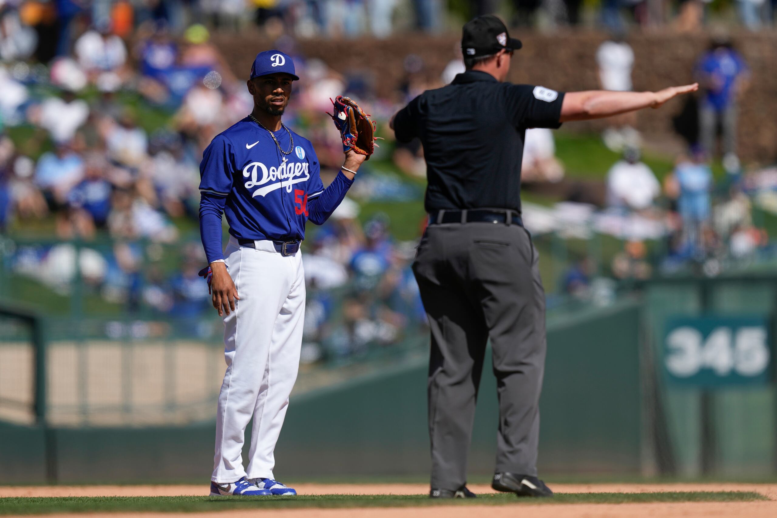 El campocorto de los Dodgers de Los Ángeles, Mookie Betts, a la izquierda, mira al umpire Quinn Wolcott mientras marca el safe de Derek Hill de los Rangers de Texas en segunda base por un error de interferencia de Betts en la quinta entrada del juego de béisbol del entrenamiento de primavera el sábado 9 de marzo de 2024, en Phoenix. (AP Foto/Carolyn Kaster)