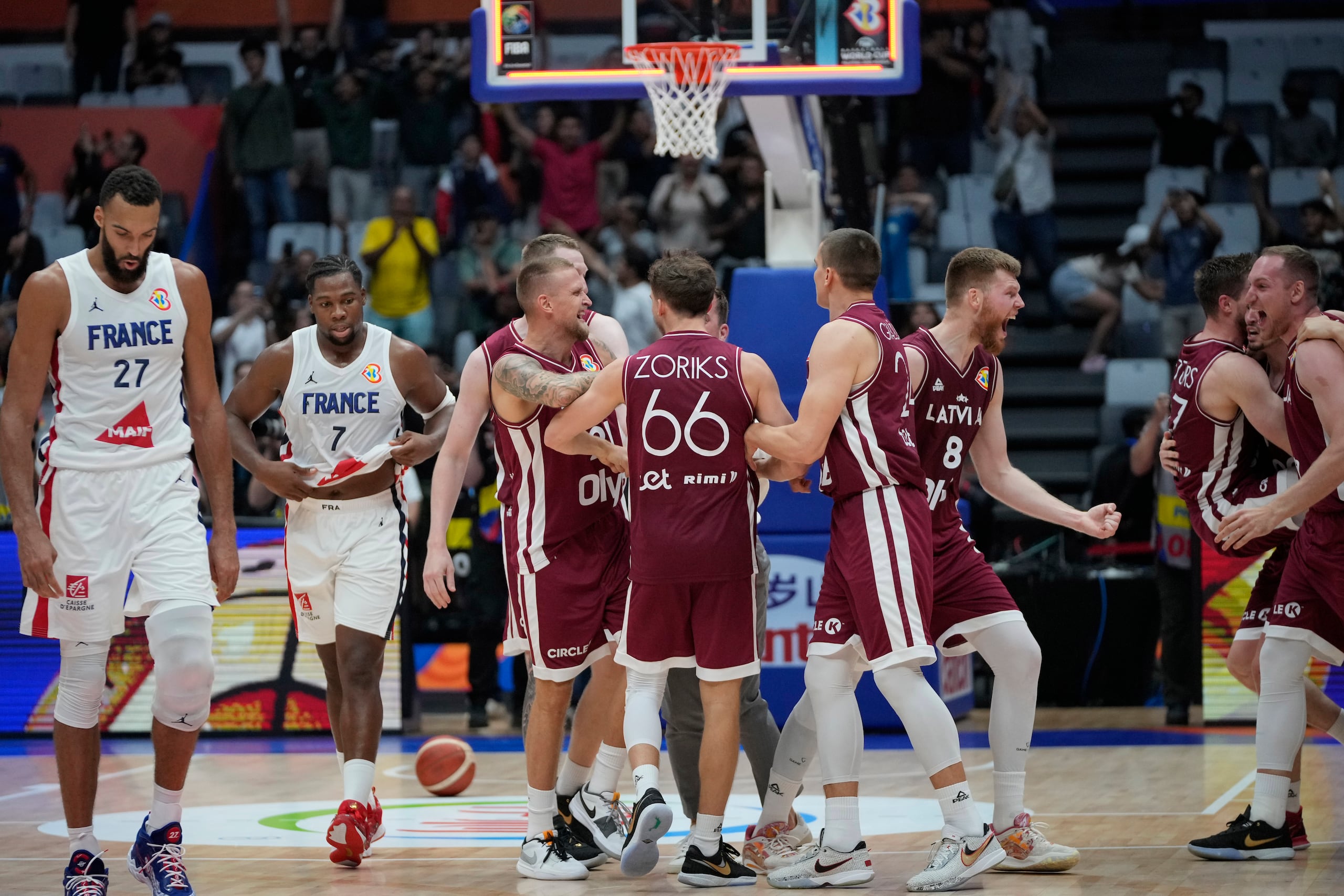 Los jugadores de Letonia celebran mientras dos canasteros de Francia comienza su agónica caminata hacia el camerino luego de sucumbir ante ellos para quedar sin opciones de clasificación a la segunda ronda de la Copa del Mundo.