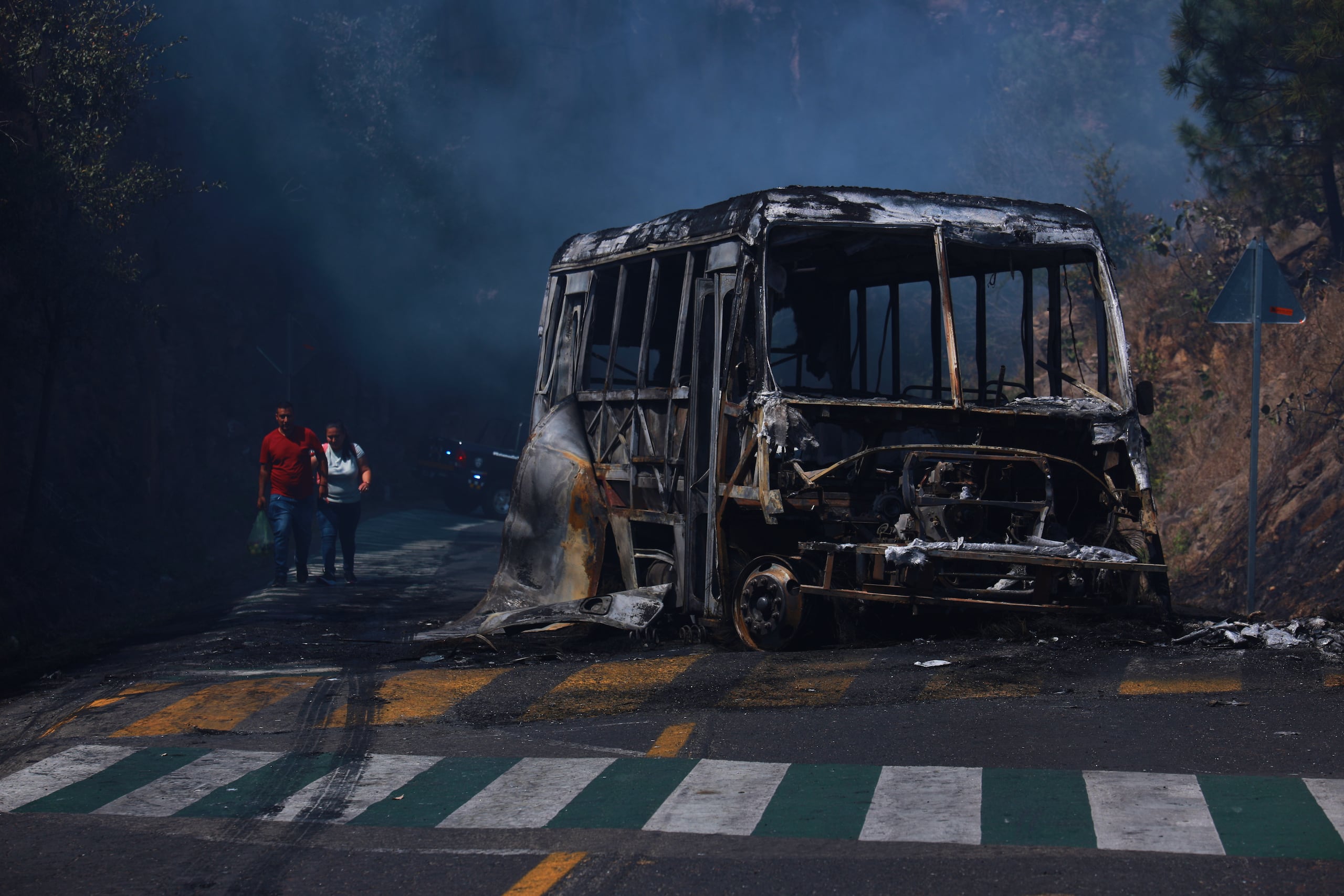 Peatones pasan junto a un autobús calcinado luego de ser incendiado en una carretera de Cointzio, Michoacán, México, el domingo 22 de febrero de 2026, tras la muerte del líder del Cártel Jalisco Nueva Generación, Nemesio Rubén Oseguera Cervantes, alias "El Mencho". (AP Foto/Armando Solís)