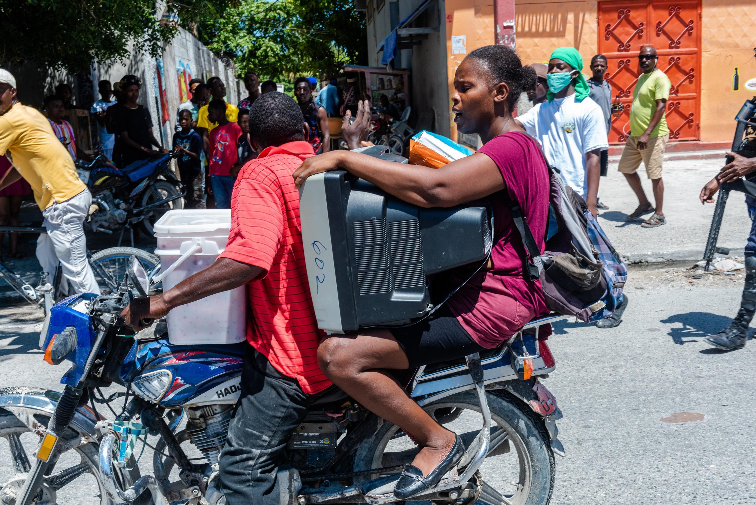 Una mujer fue registrada este viernes al llevar un televisor y otras pertenencias mientras huye en una motocicleta de la violencia de las bandas armadas, en Puerto Príncipe, Haití.