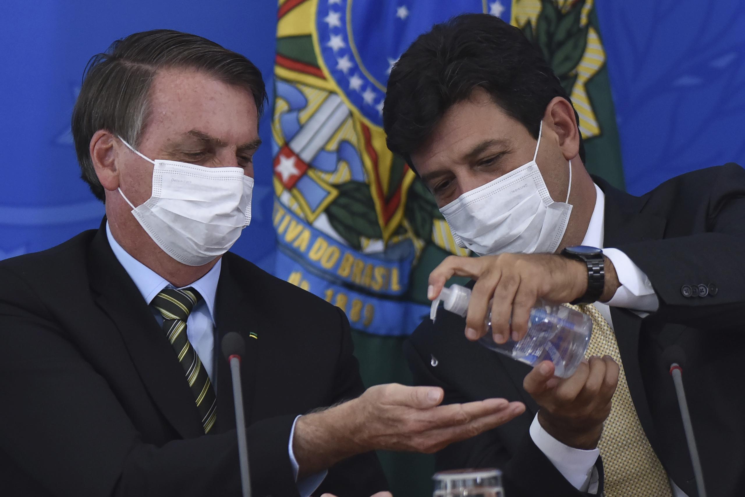 El ministro de salud de Brasil Luiz Henrique Mandetta, derecha, aplica desinfectante en las manos al presidente Jair Bolsonaro durante una conferencia de prensa en el Palacio Presidencial de Planalto en Brasilia