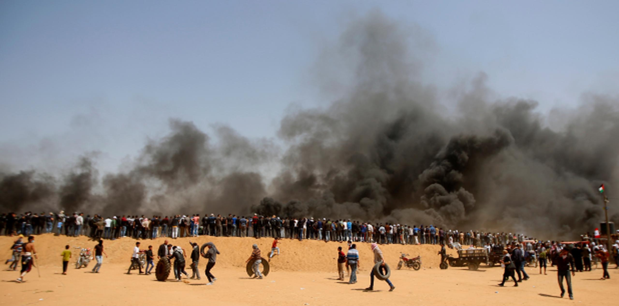 Manifestantes palestinos esperan en una duna de arena mientras otros trasladan neumáticos para quemarlos durante enfrentamientos con tropas israelíes junto a la frontera entre la Franja de Gaza e Israel. (AP)