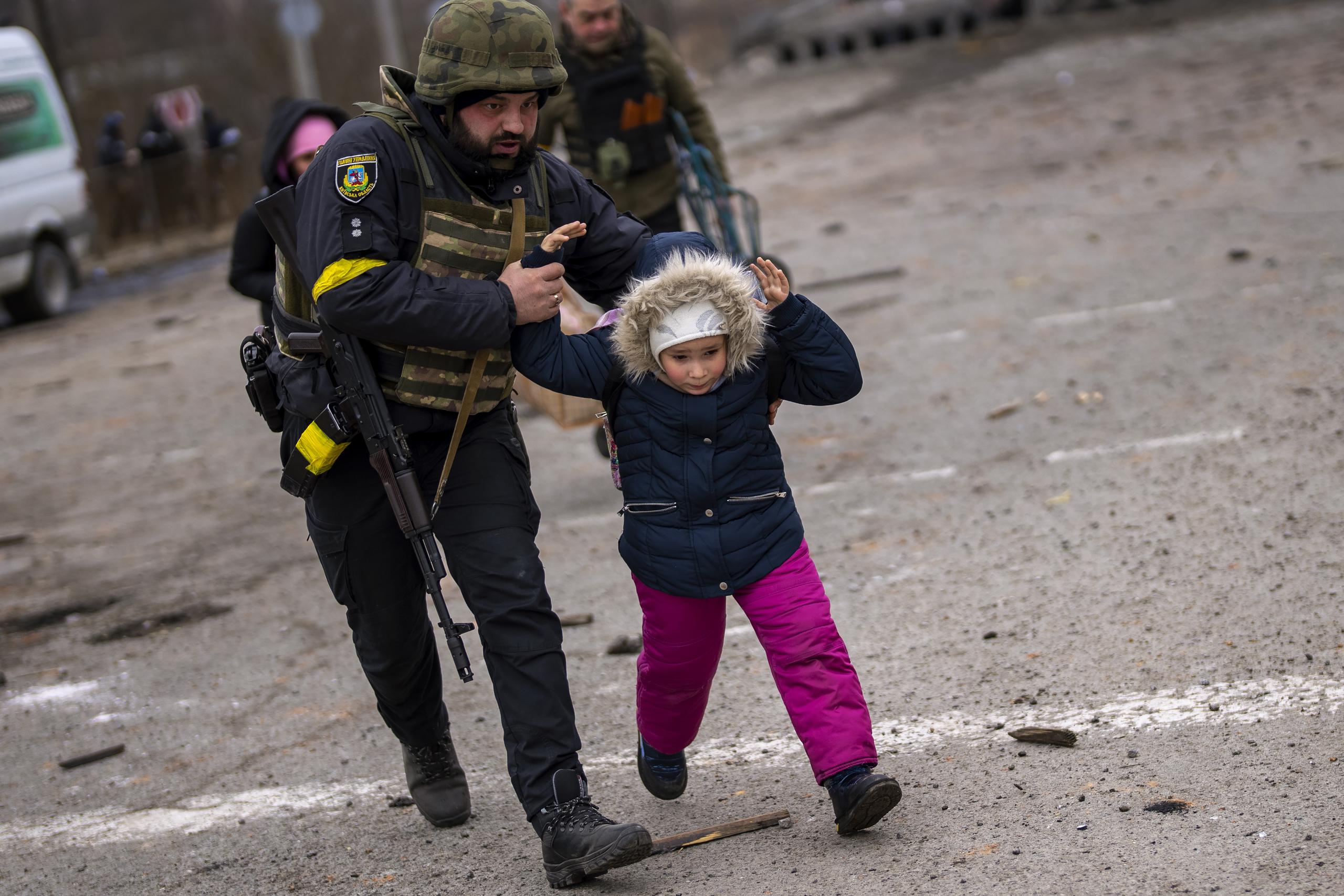 Un policía ucraniano ayuda a una niña que corre ante los estallidos de artillería cercana, mientras la población civil abandona Irpin, en las afueras de Kiev, Ucrania, el lunes 7 de marzo de 2022. (AP Foto/Emilio Morenatti)