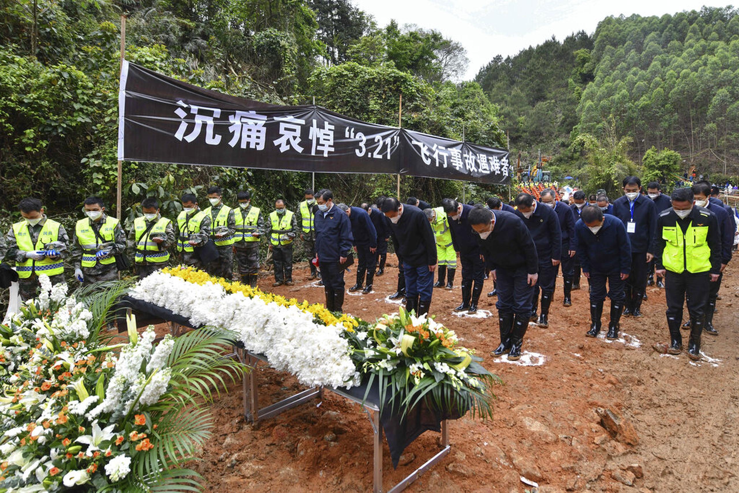 Funcionarios y trabajadores de búsqueda y rescate hacen una pausa de tres minutos de silencio por las 132 personas muertas en el lugar donde se accidentó el avión de China Eastern, el 27 de marzo de 2022.