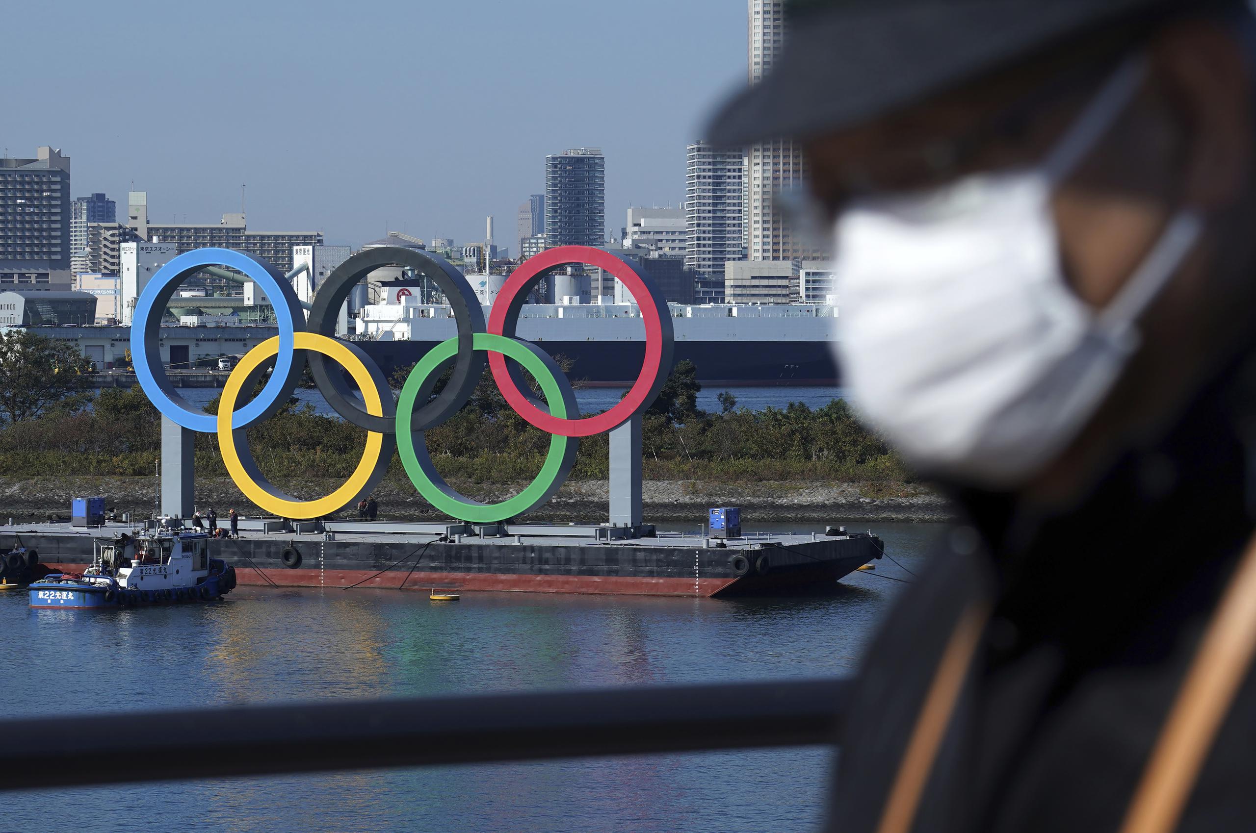 Un hombre con tapabocas pasa frente a los anillos olímpicos en Tokio. Un rebrote del coronavirus hace que surjan dudas acerca de la realización de los Juegos Olímpicos a mediados del año.