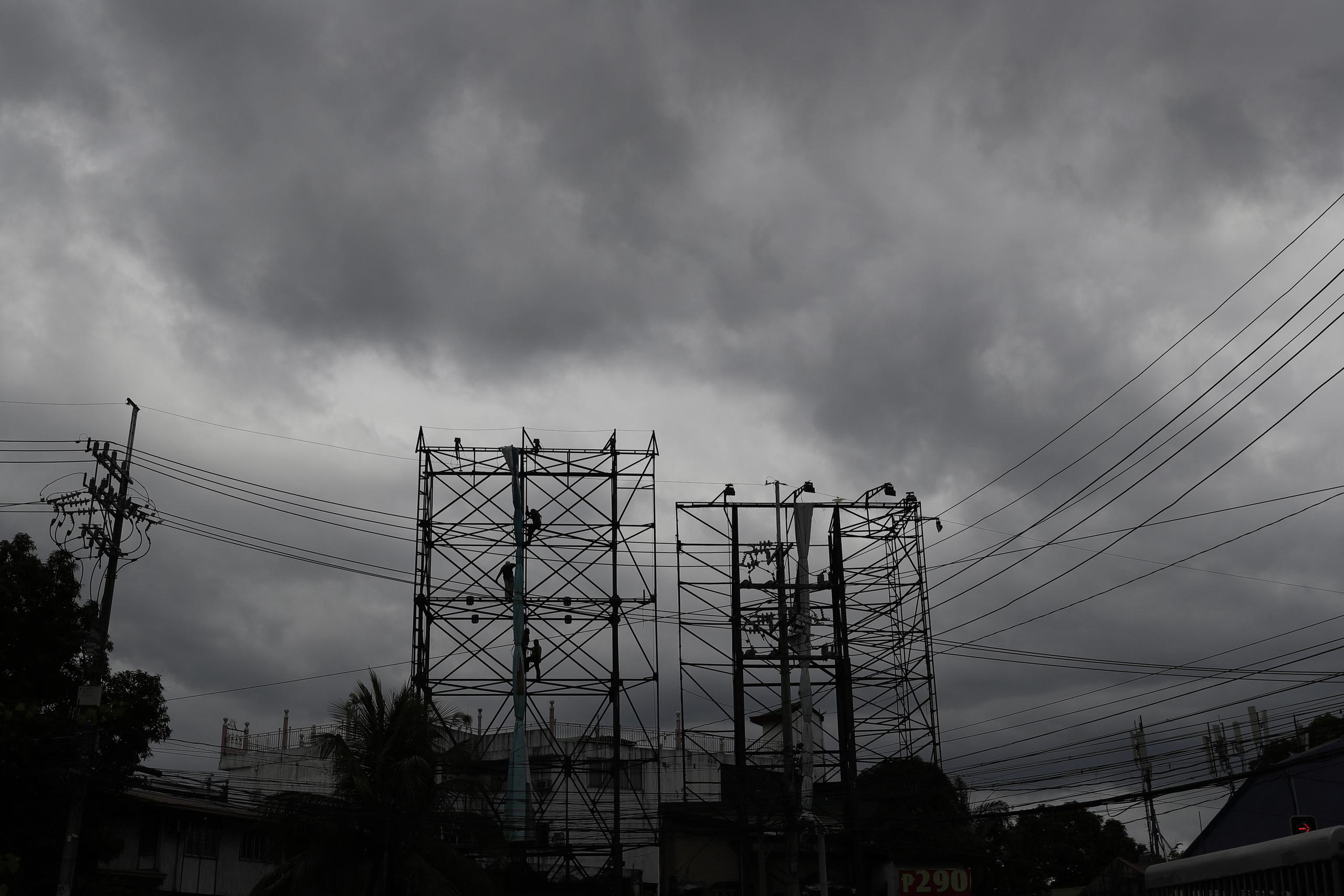 Nubes negras cubren el cielo mientras operarios retiran un cartel antes de la llegada del tifón Vongfong, en Manila, Filipinas