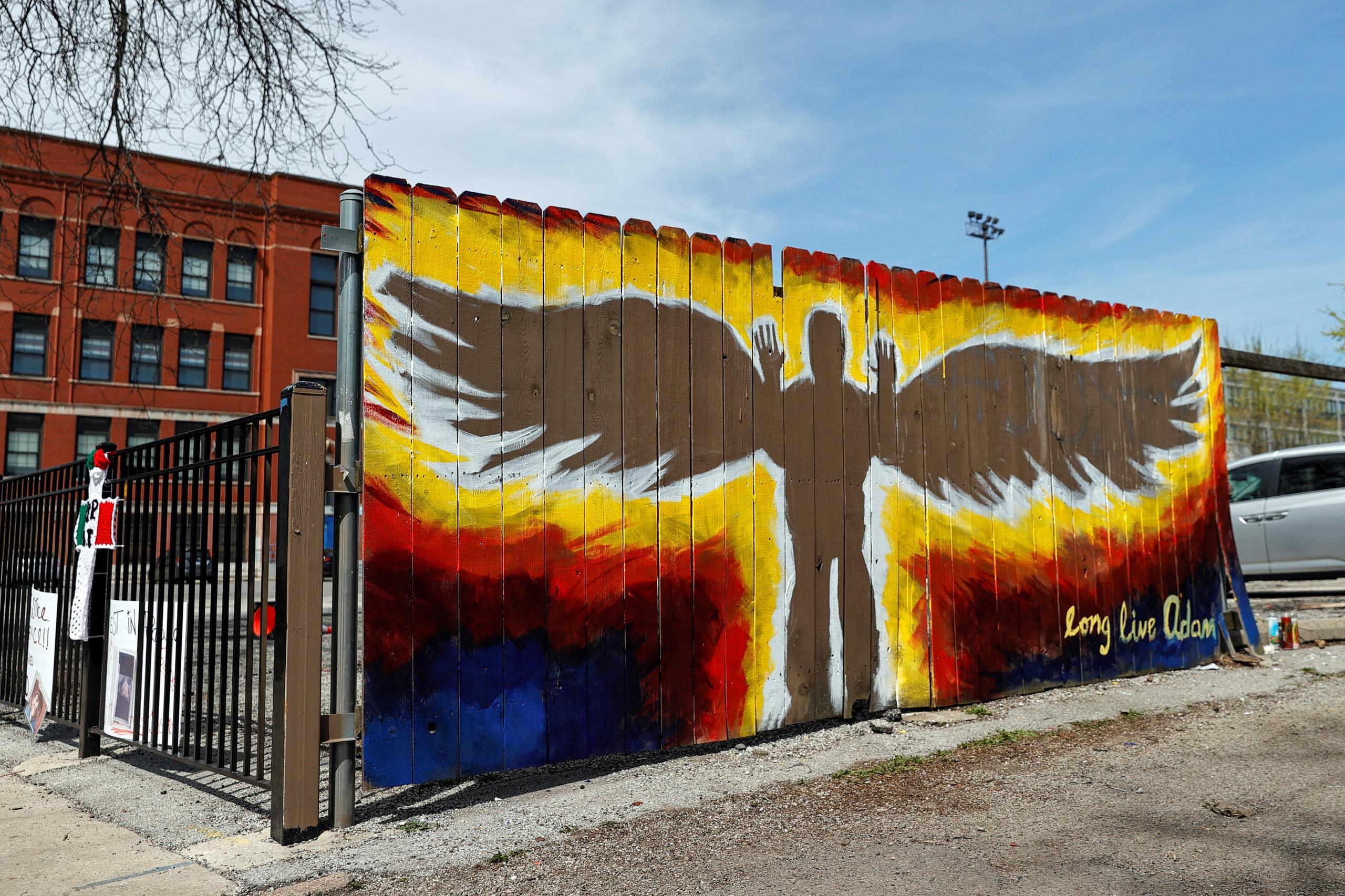 Vista de un mural con el dibujo de una persona con alas y las manos en alto y la frase ""Larga Vida a Adam"" instalado frente a un pequeño altar improvisado en memoria del joven Adam Toledo en el vecindario de La Villita en Chicago, Illinois.
