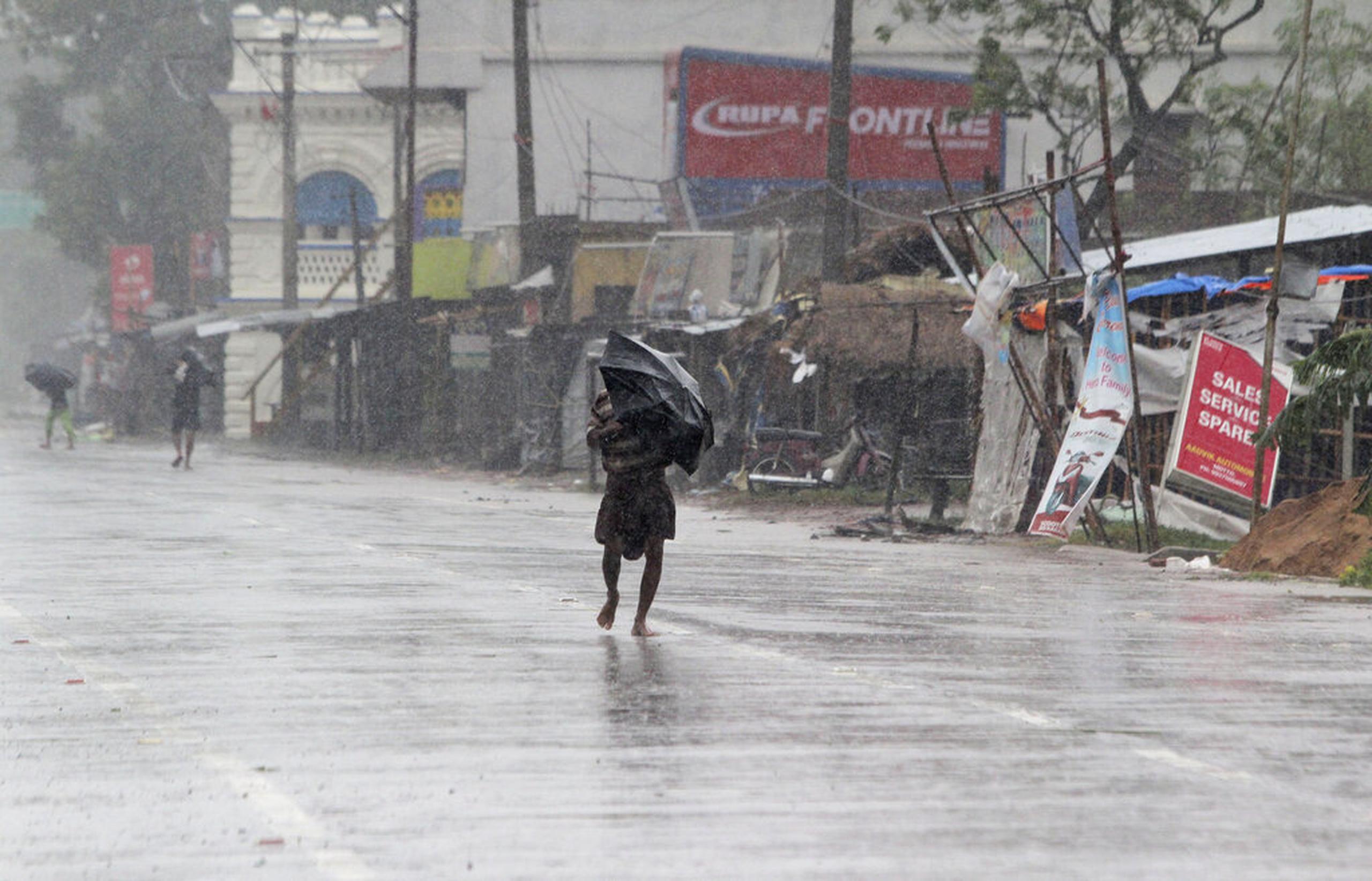Personas caminaban hoy con sombrillas bajo la lluvia antes de que Amphan tocara tierra, en el distrito de Bhadrak, en el estado indio oriental de Orissa.