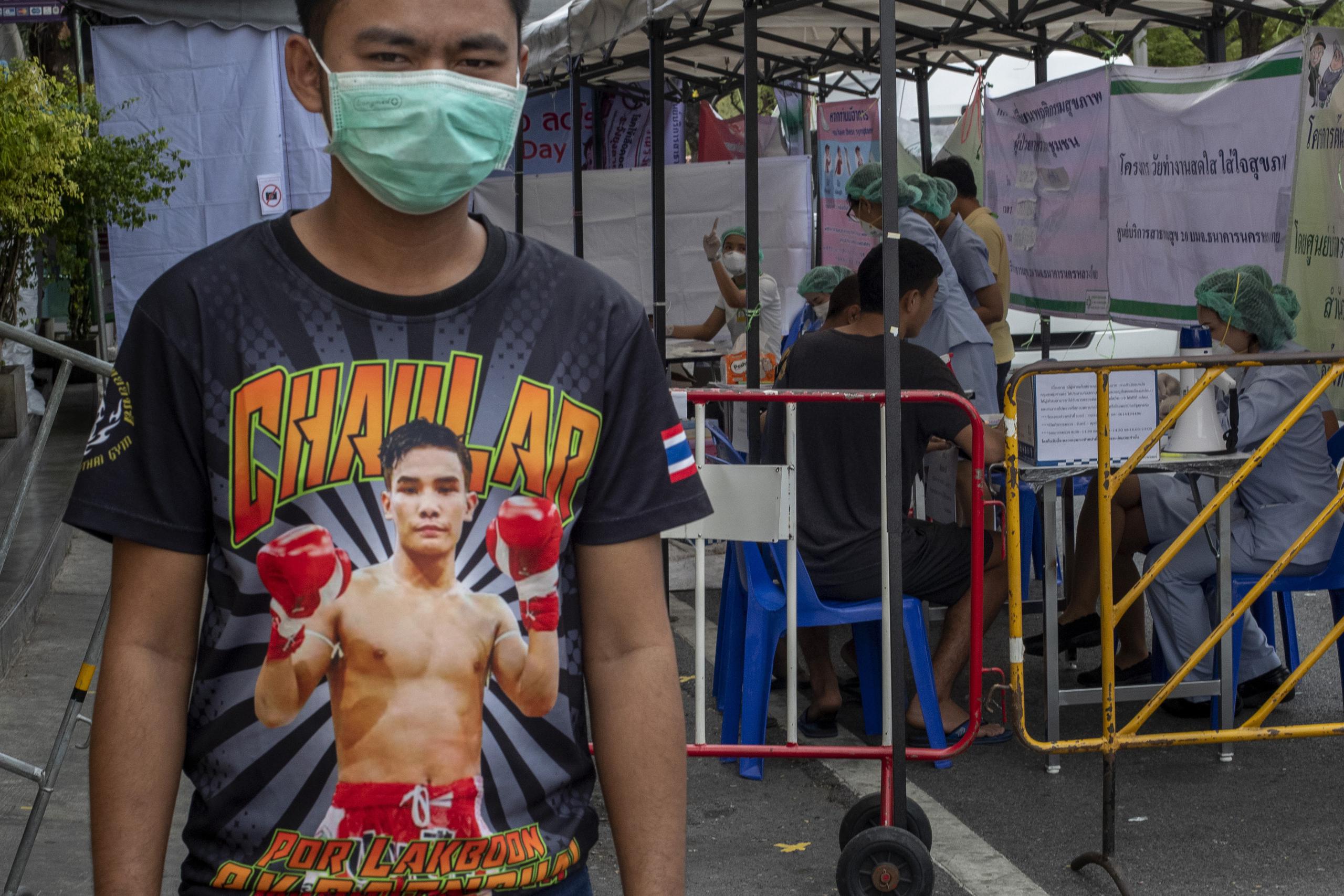En esta fotografía del jueves 19 de marzo de 2020, un peleador de muay thai observa frente a un puesto improvisado para detectar el coronavirus afuera del estadio de boxeo Rajadamnern en Bangkok, Tailandia.
