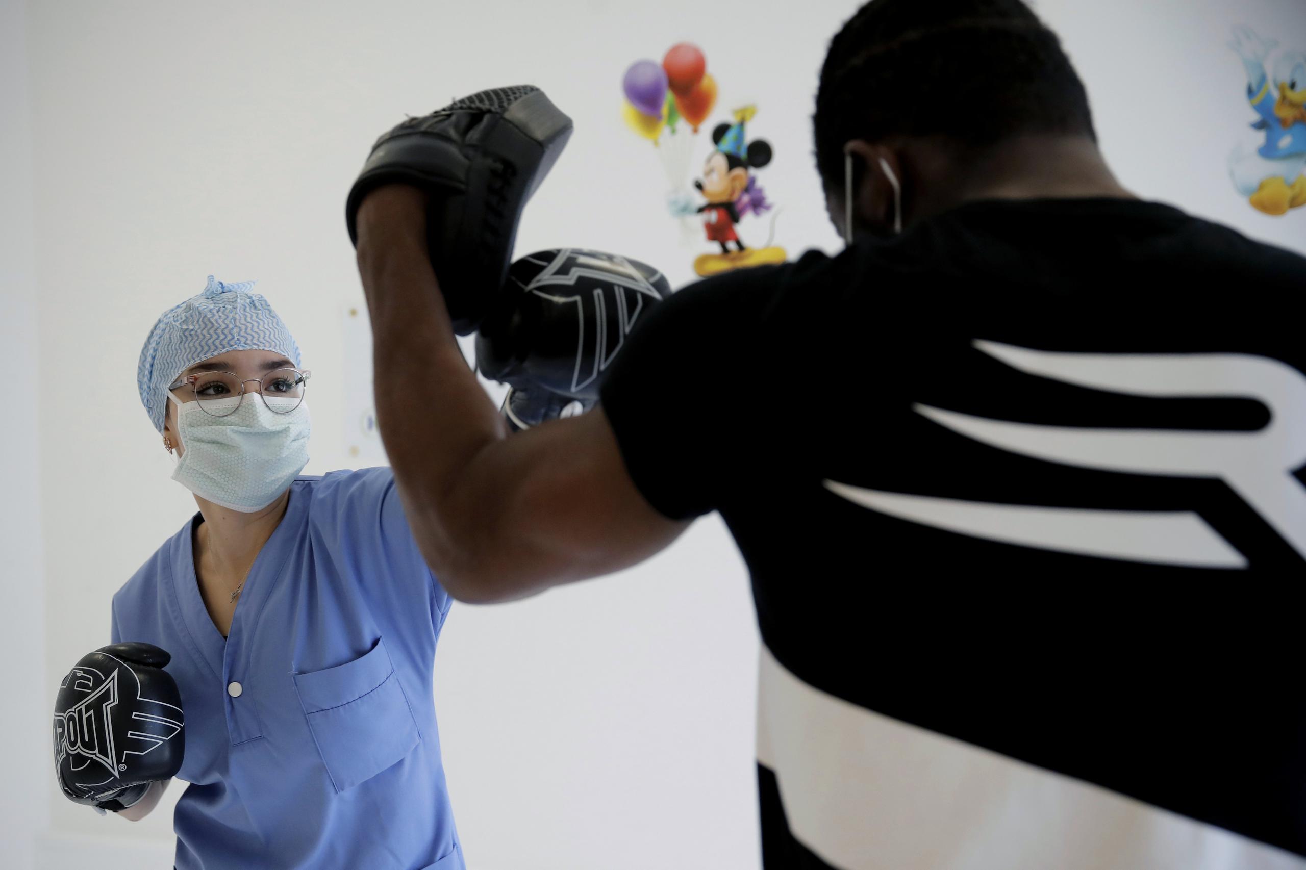 La enfermera Nassima Guermat suelta su mano izquierda durante una sesión de entrenamiento con el excampeón mundial de boxeo Hassan N'Dam en el hospital Villeneuve-Saint-Georges de las afueras de París. (AP)