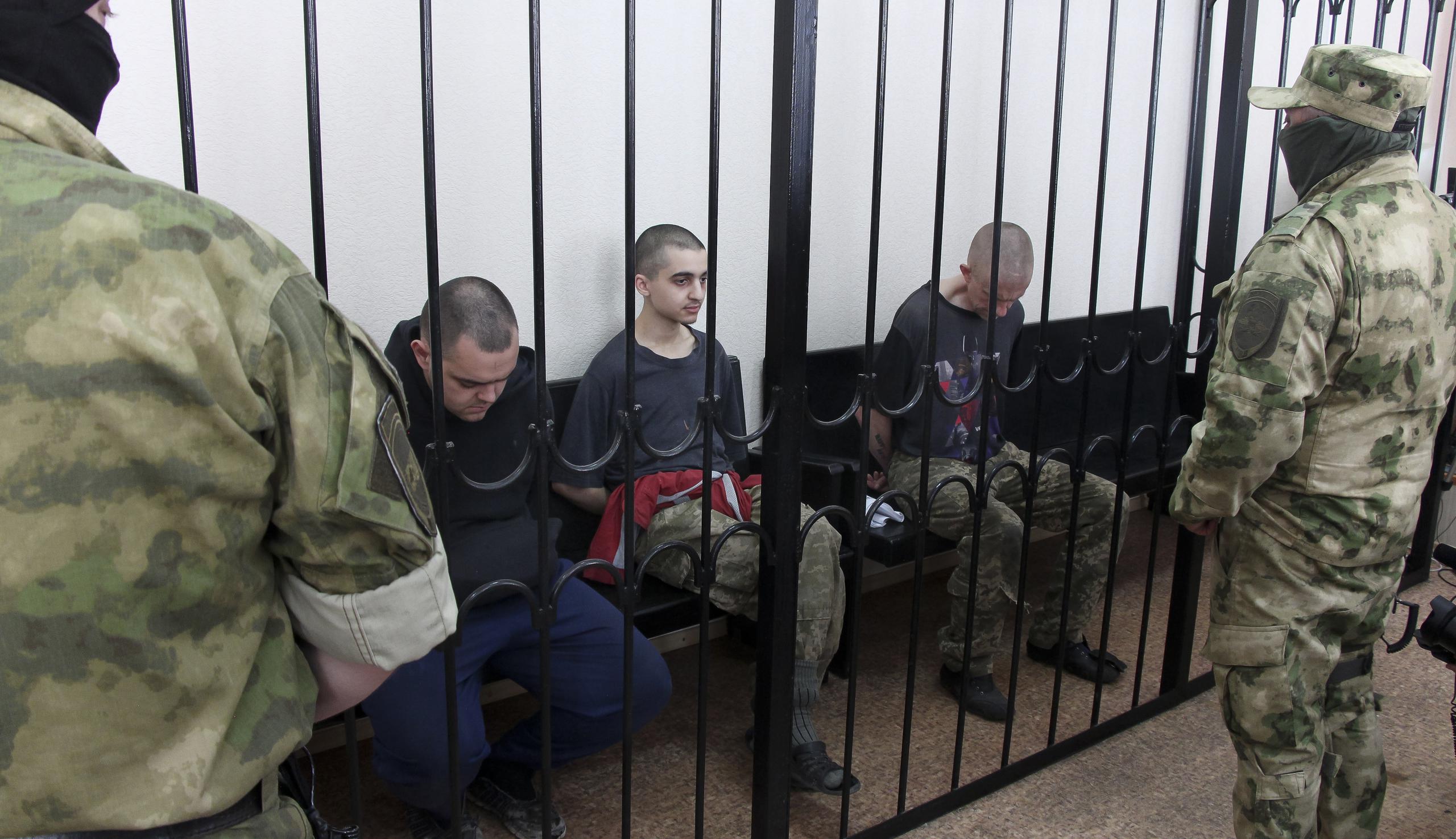 Dos ciudadanos británicos, Aiden Aslin (izquierda) y Shaun Pinner (derecha), y el marroquí Saaudun Brahim (centro) se sientan tras las rejas en una sala de audiencias en Donetsk, en el territorio que está bajo el control del Gobierno de la República Popular de Donetsk, en el este de Ucrania. Jueves, 9 de junio de 2022. Los dos ciudadanos británicos y un marroquí han sido condenados a muerte por rebeldes pro-Moscú en el este de Ucrania por luchar del lado de Ucrania. Los tres hombres lucharon junto a las tropas ucranianas y se rindieron a las fuerzas rusas hace semanas. (Foto AP)