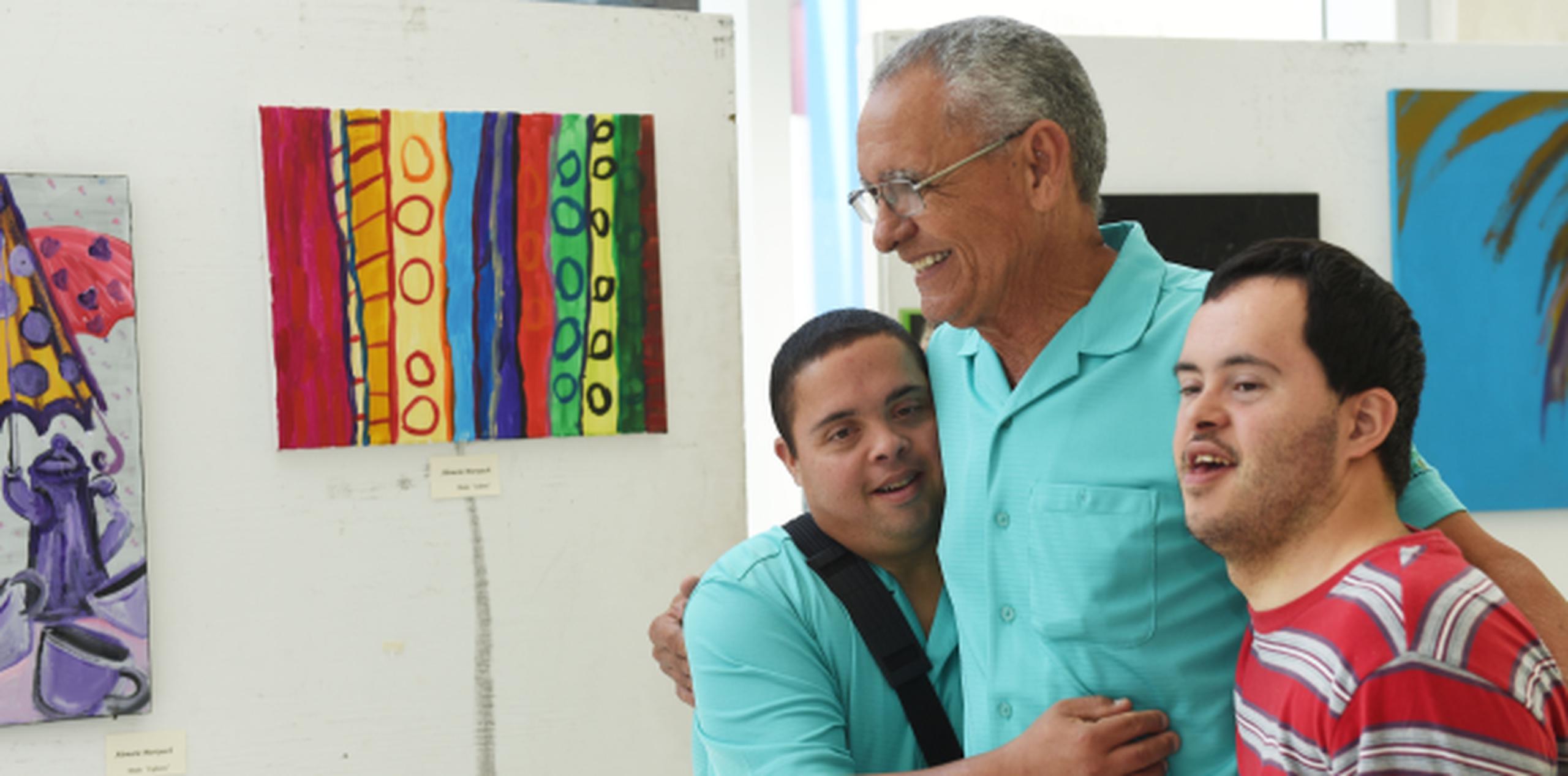 Unos sonrientes Omar Meléndez (24) y Axel Martínez (41), abrazan a Henry Martínez, de la Fundación Puertorriqueña Síndrome Down, al presentar sus obras durante el Simposio de la Familia. (tony.zayas@gfrmedia.com)