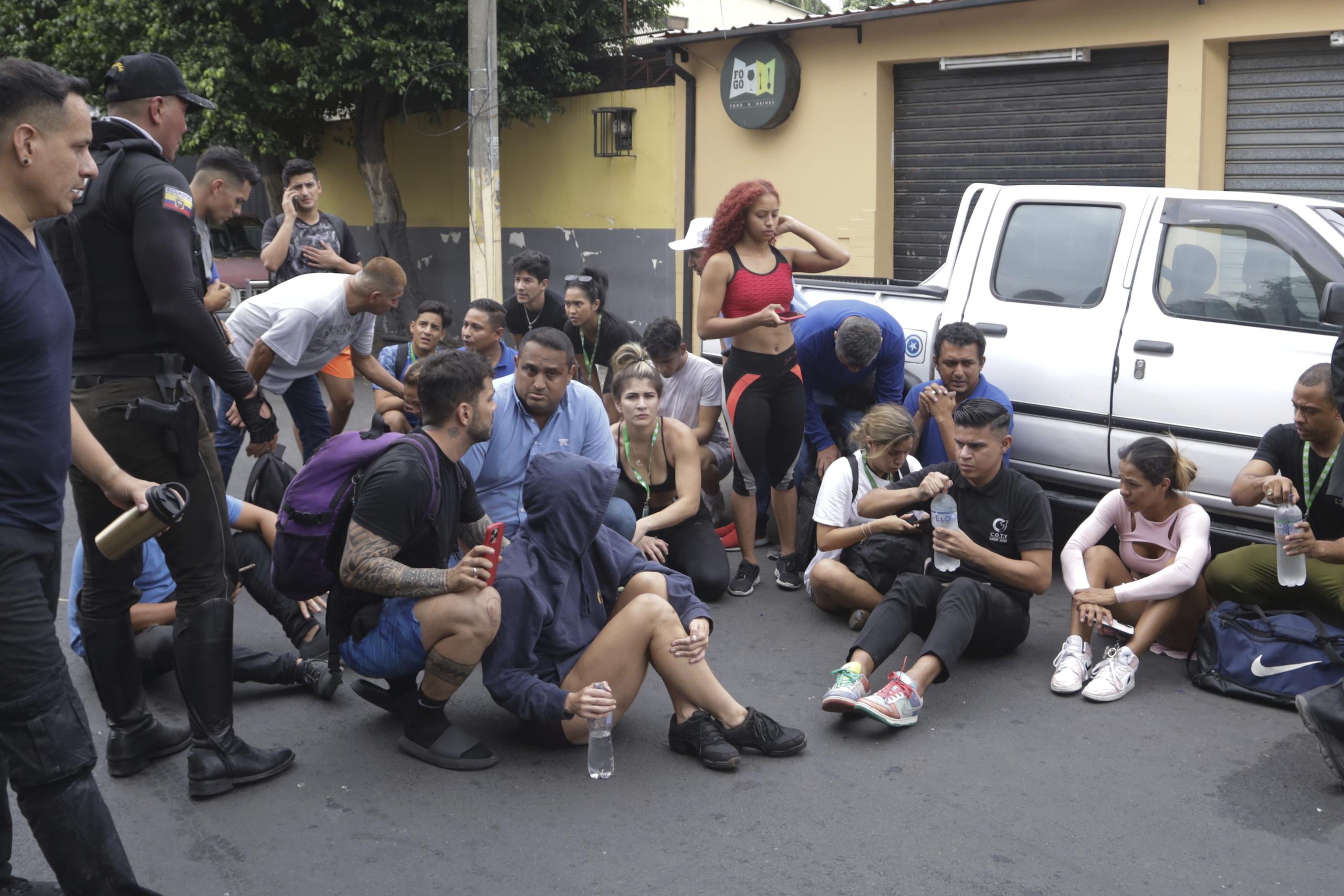 Personal del canal TC Televisión sentados en el suelo en la calle tras ser evacuados después de que un grupo armado y encapuchado irrumpiera en plena transmisión en directo, en Guayaquil, Ecuador, el 9 de enero de 2024.