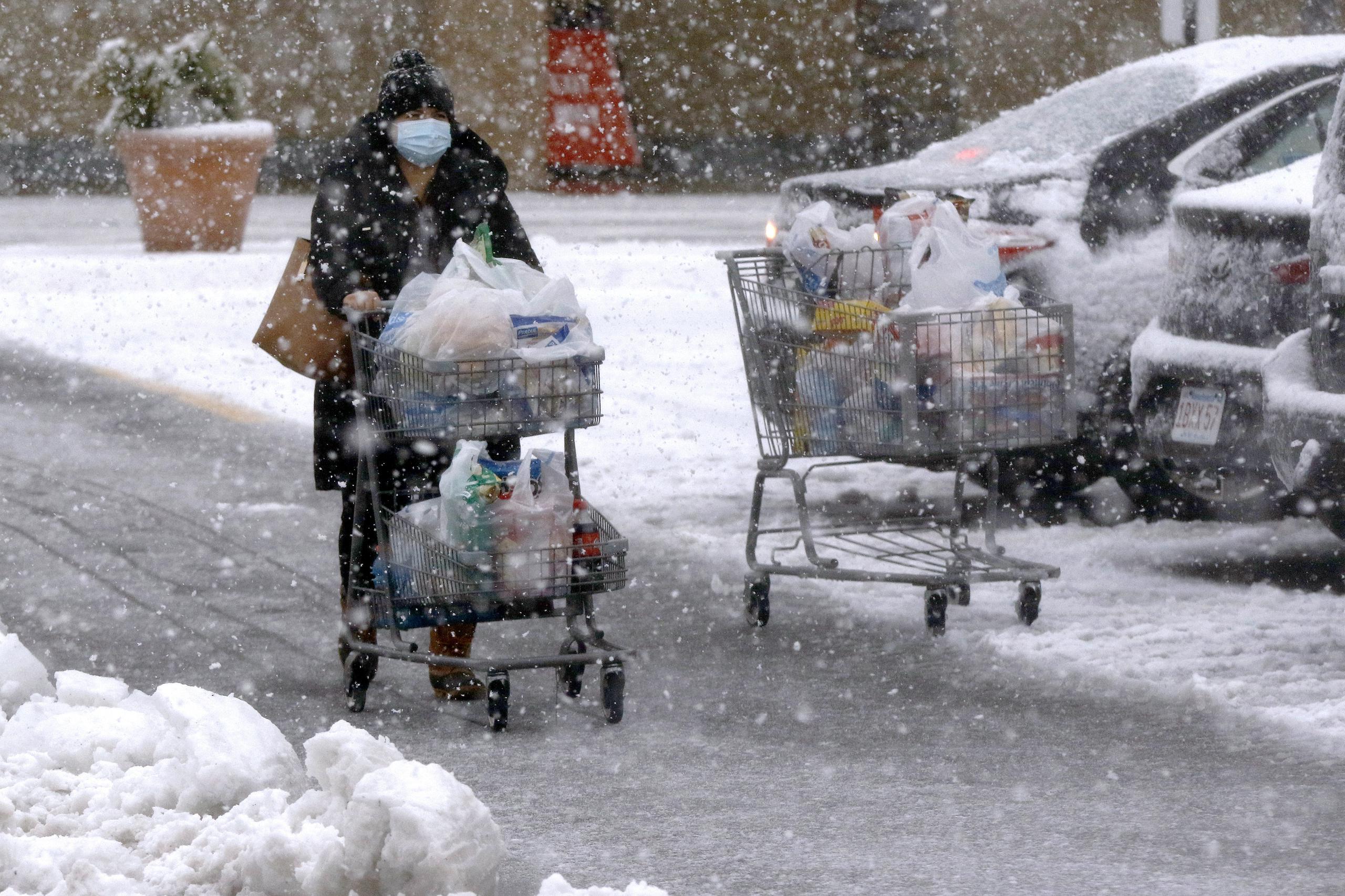 Una persona transporta comestibles en un carrito bajo una fuerte nevada en un estacionamiento en Marlborough, Massachusetts.