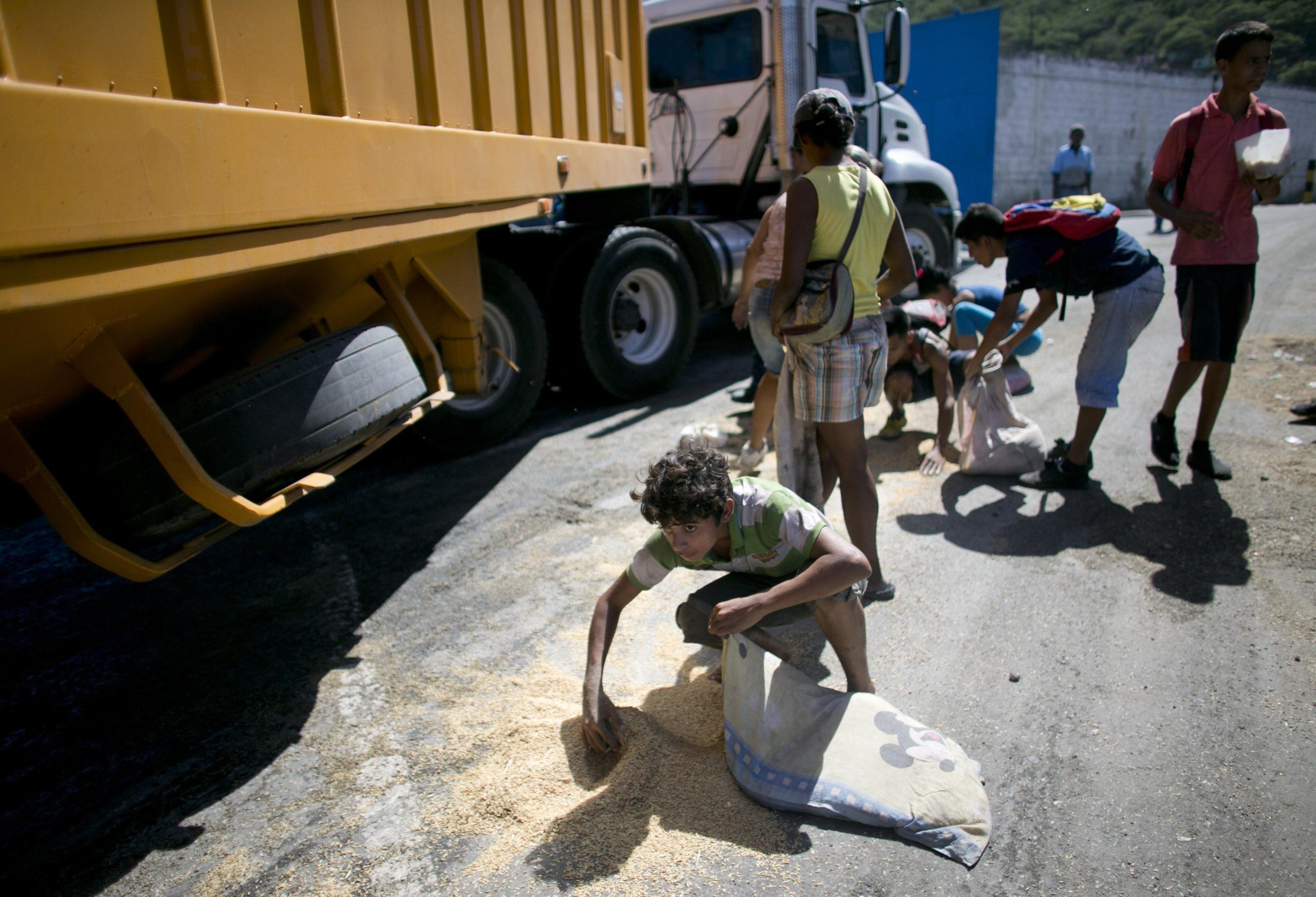 Un joven utiliza una funda almohada como bolsa para recoger arroz del piso, caído de un camión de mercancías que esperaba para entrar al puerto de Puerto Cabello, en Venezuela. (AP)