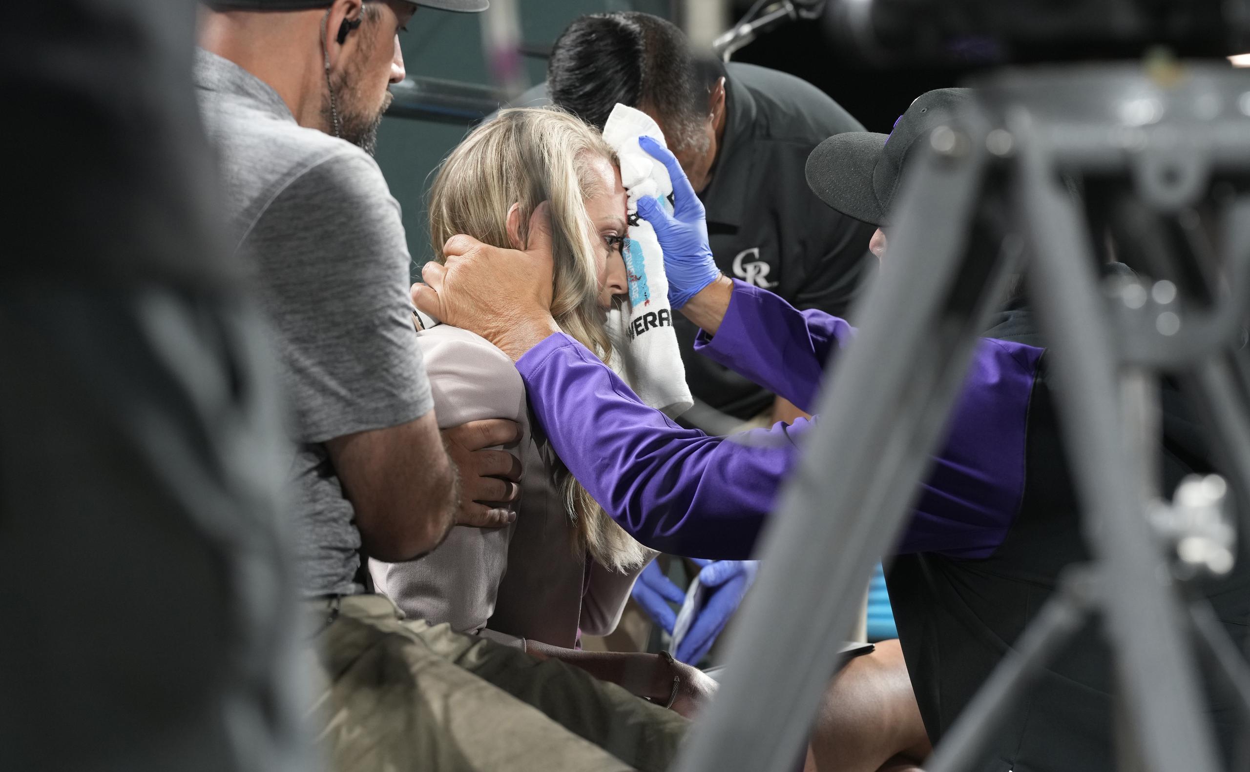 Kelsey Wingert, reportera de televisión de los Rockies de Colorado, recibe atención luego de que una pelota bateada de foul la golpeó en la frente durante el juego del 16 de mayo de 2022, en Denver.
