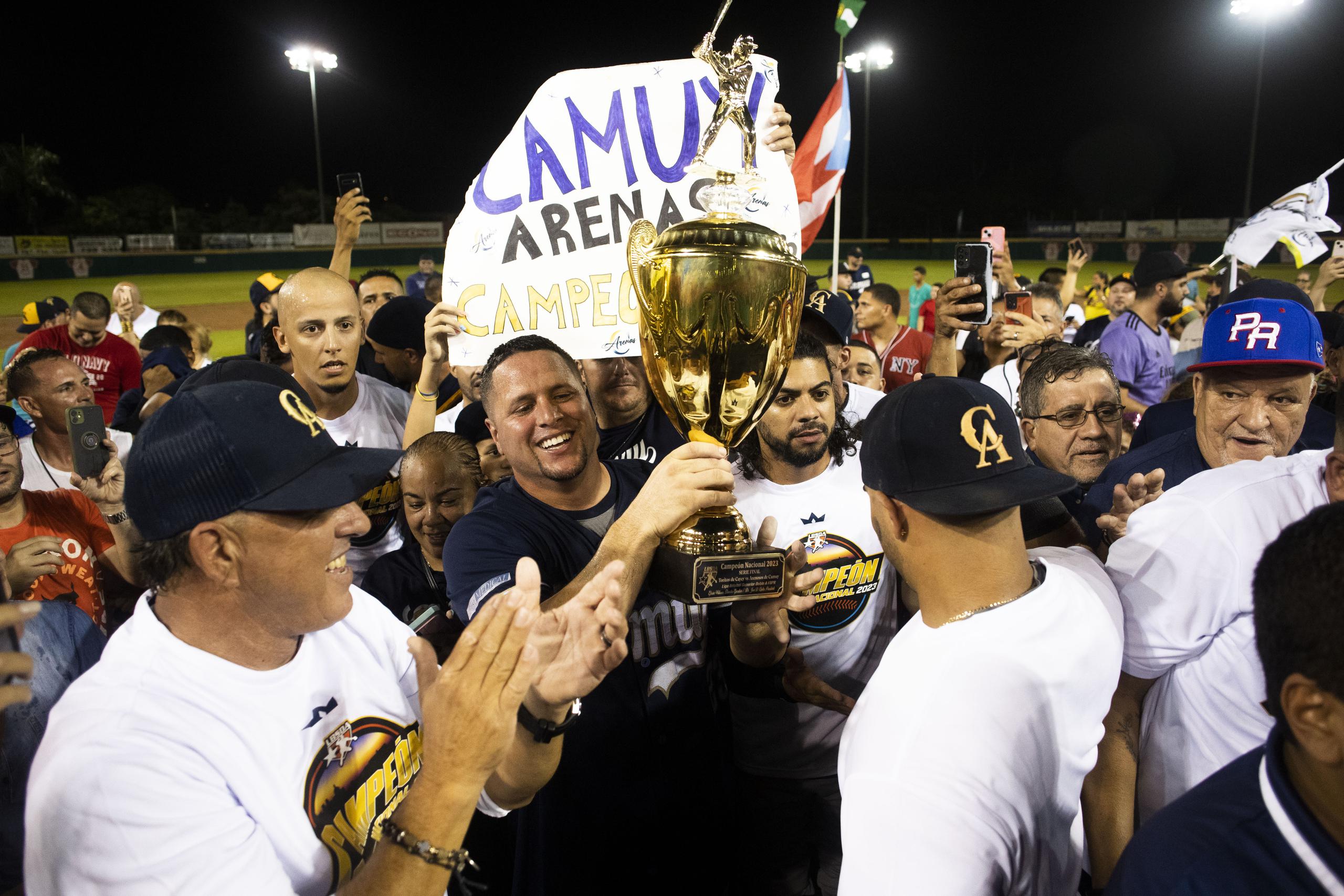 El dirigente-jugador Dennis Pérez levanta el trofeo de campeón rodeado de la administración de los Arenosos tras ganó el domingo su primer título en la Doble A.